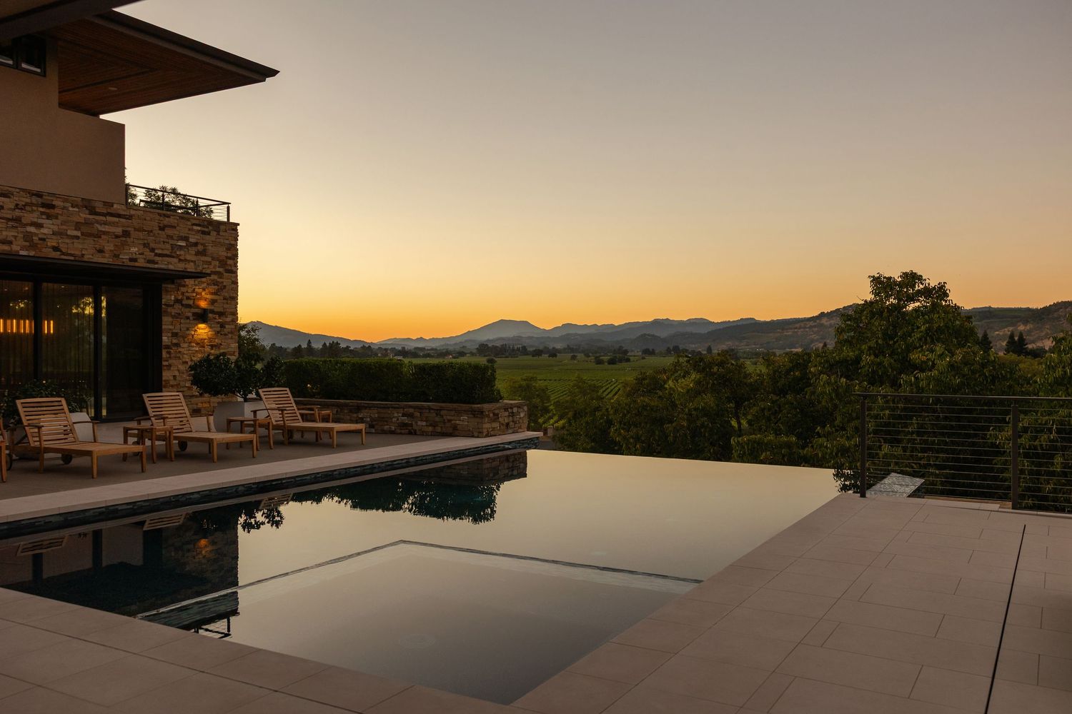 Modern infinity pool overlooking vineyard landscape at sunset.