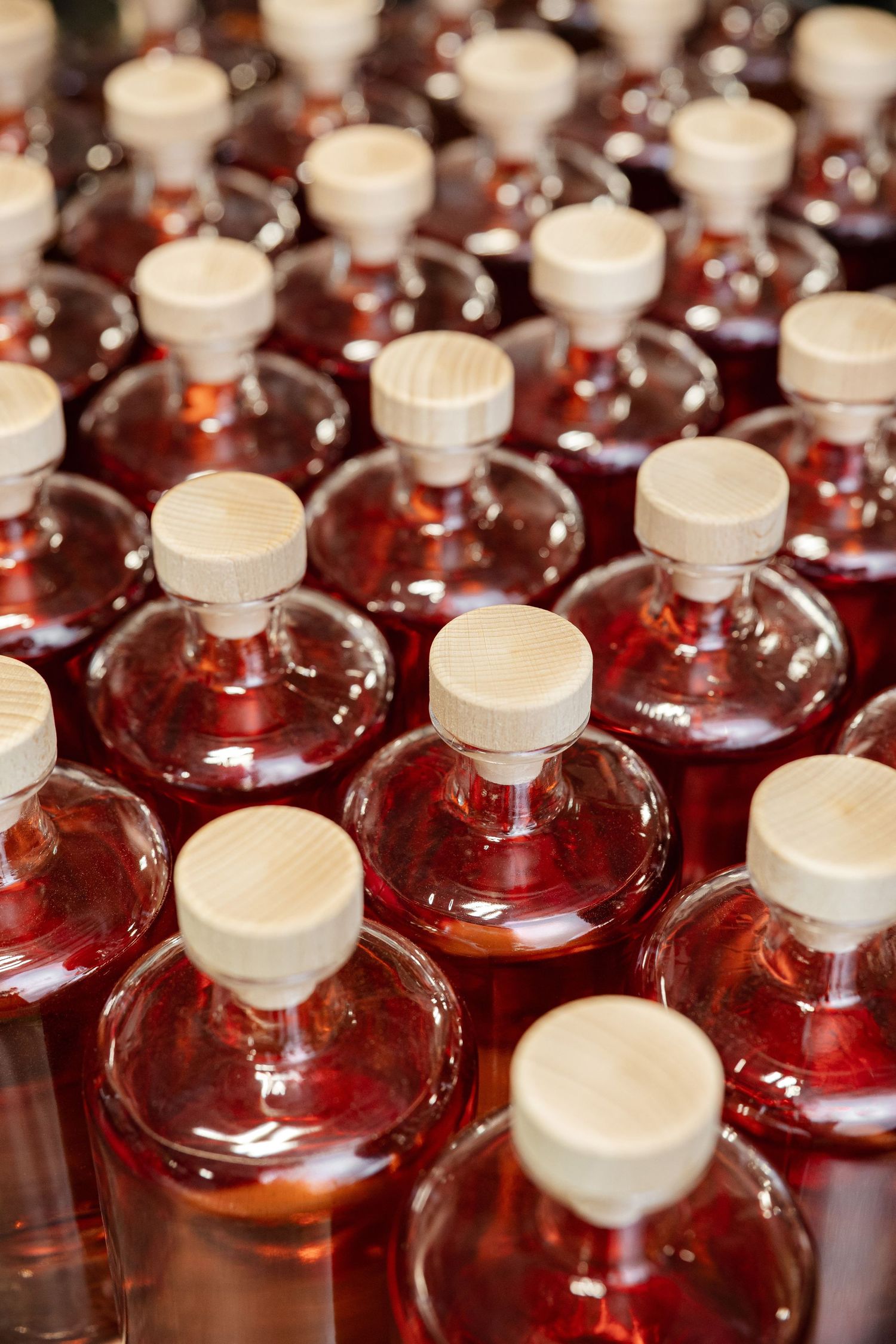 Rows of glass bottles filled with pink liquid and white caps arranged in uniform pattern.