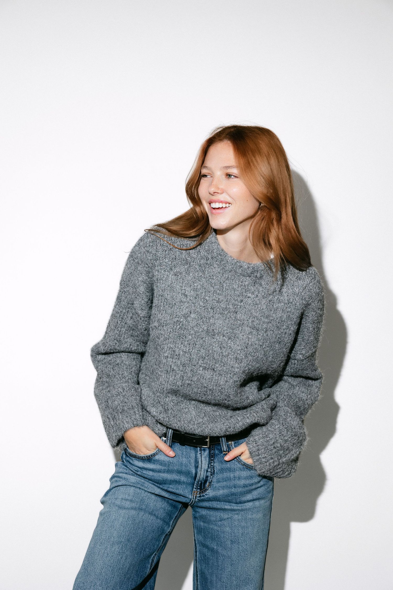 Fashion photo showing cozy grey sweater and blue jeans outfit against white background.