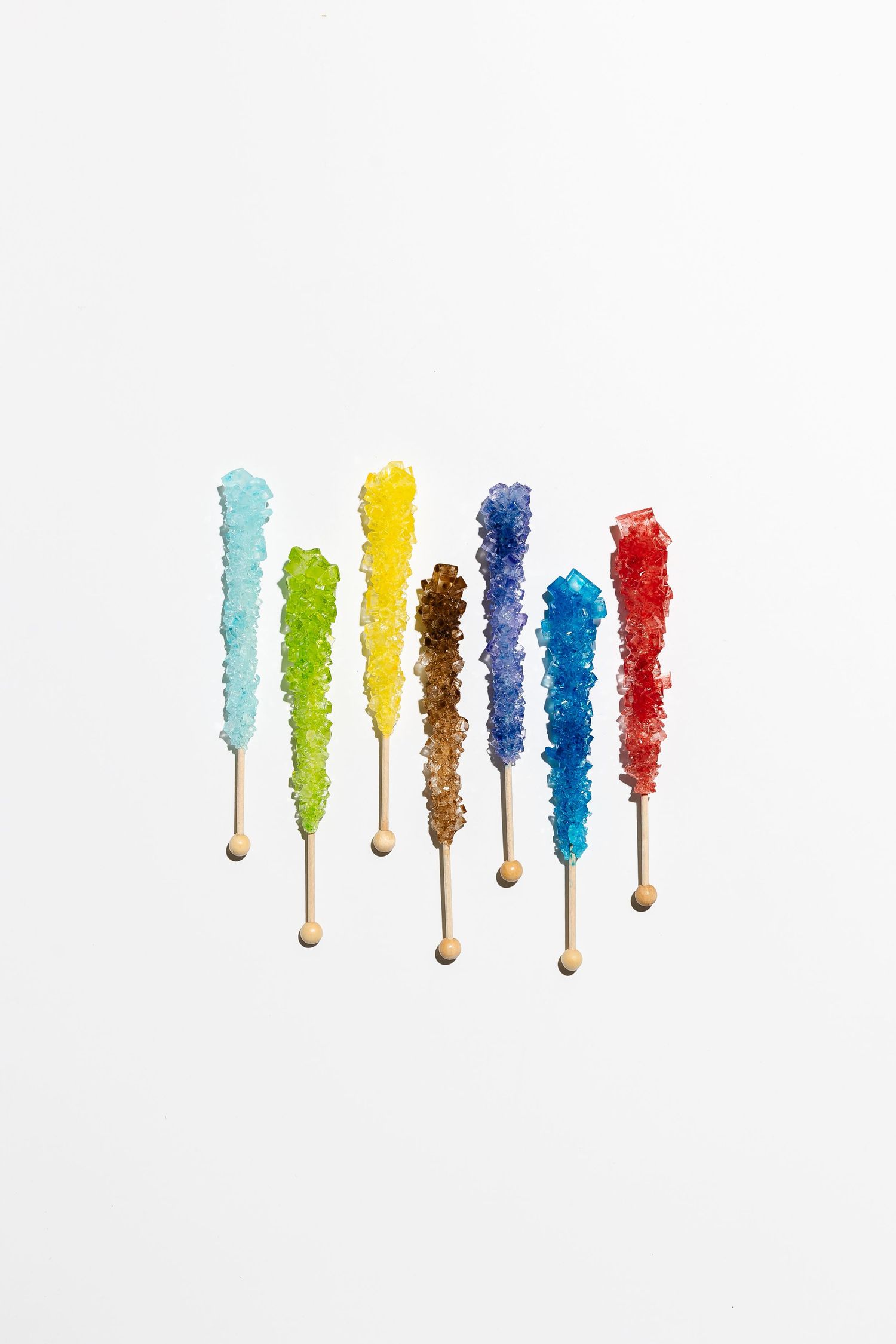 Colorful rock candy sticks arranged in a row showing different vibrant hues against white background.