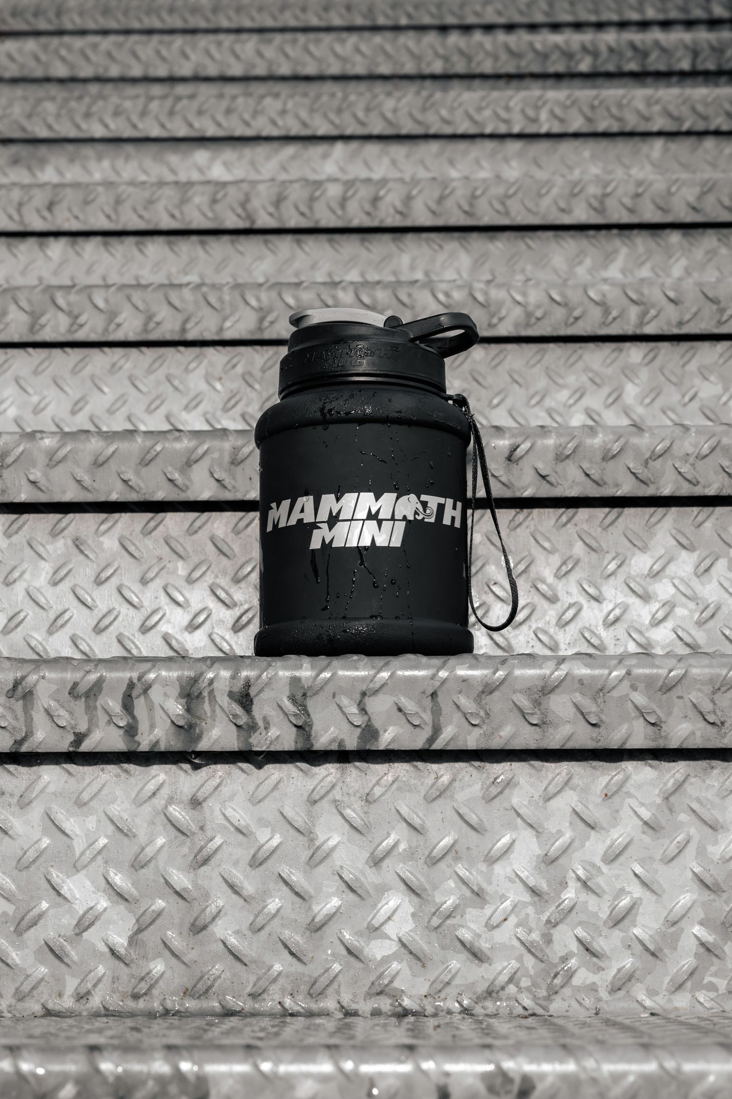 Black Mammoth branded water bottle displayed on metal diamond plate surface.