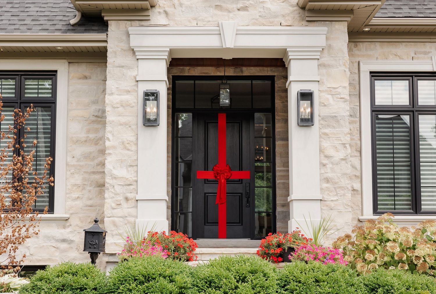 Modern stone house entrance featuring black door decorated with large red cross design.