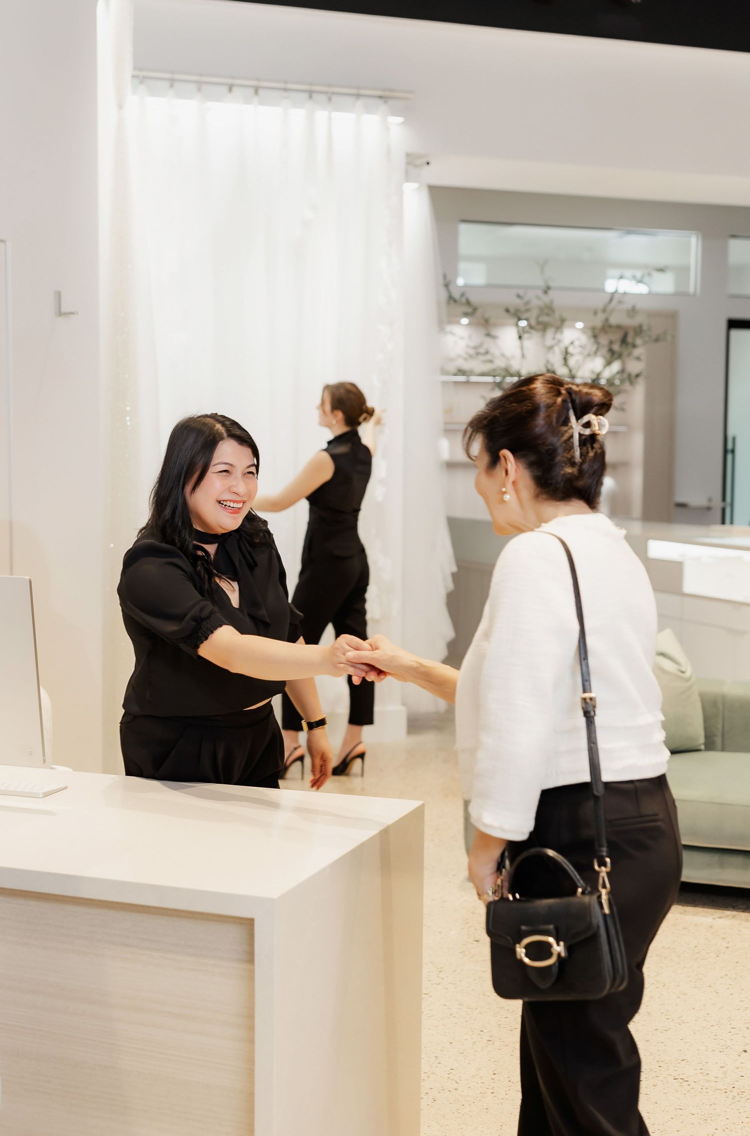 Staff members engage with customers at a sleek white retail counter in a bright store environment.