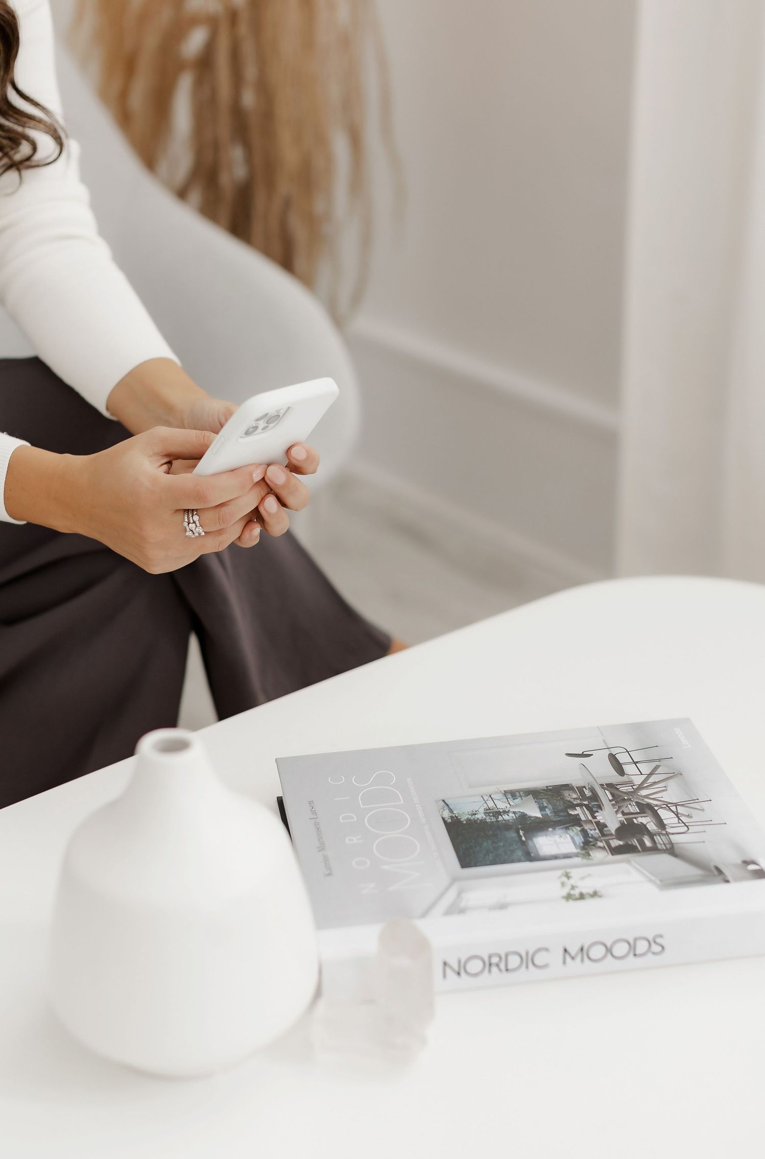 Minimalist workspace scene with hands flipping through a Nordic design book on a white desk.