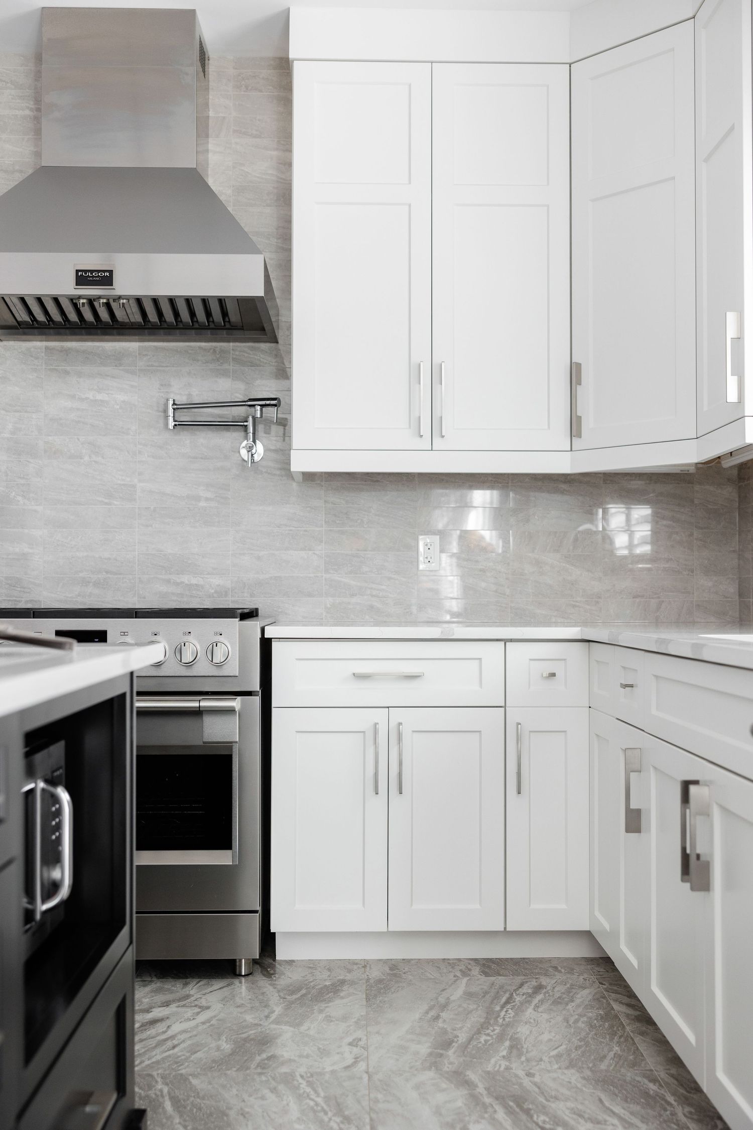 Sleek white kitchen cabinets with stainless steel appliances and gray marble flooring.