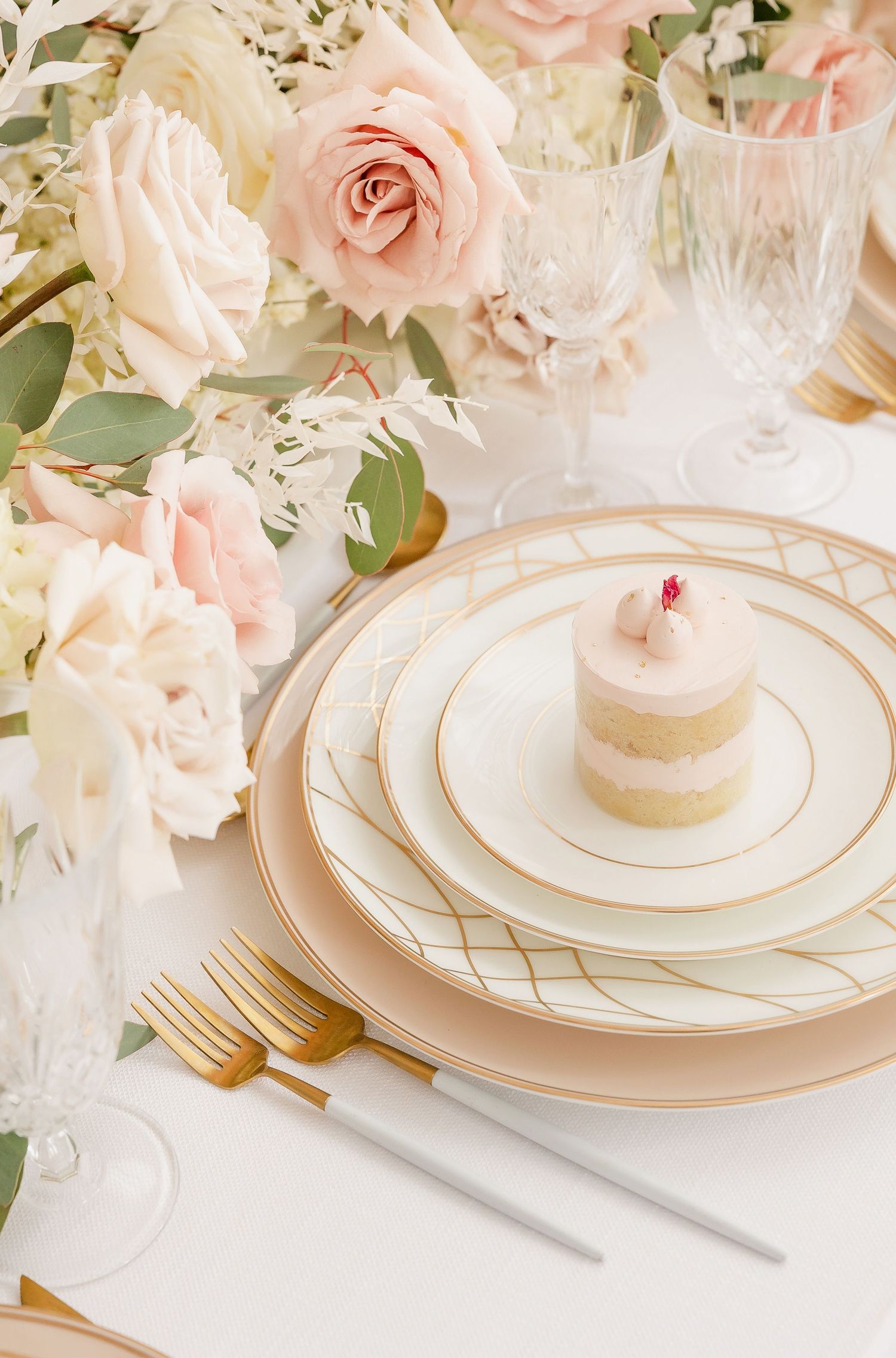 Luxurious table setting with layered plates, gold trim, and soft pink roses.