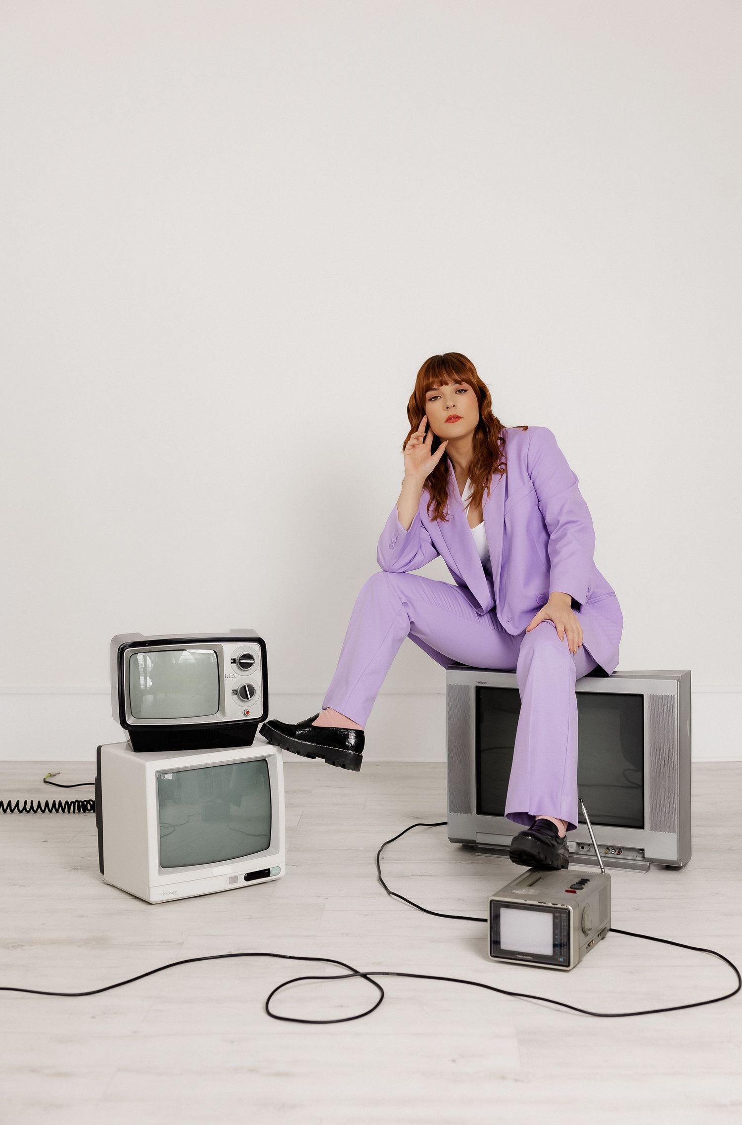Retro television sets arranged with model in lavender pantsuit against white background.