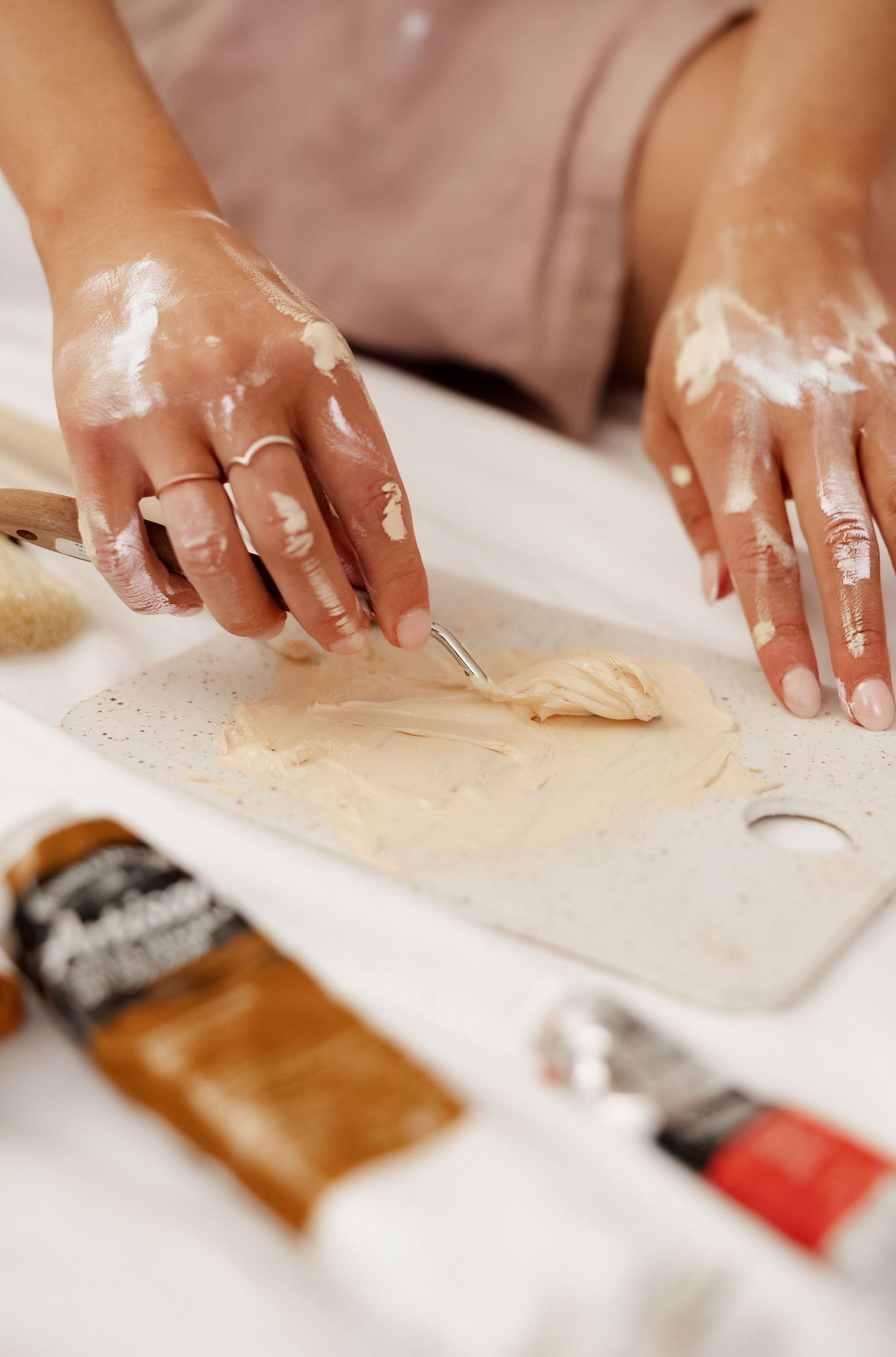 Close-up of hands working with clay or artistic materials on white surface.