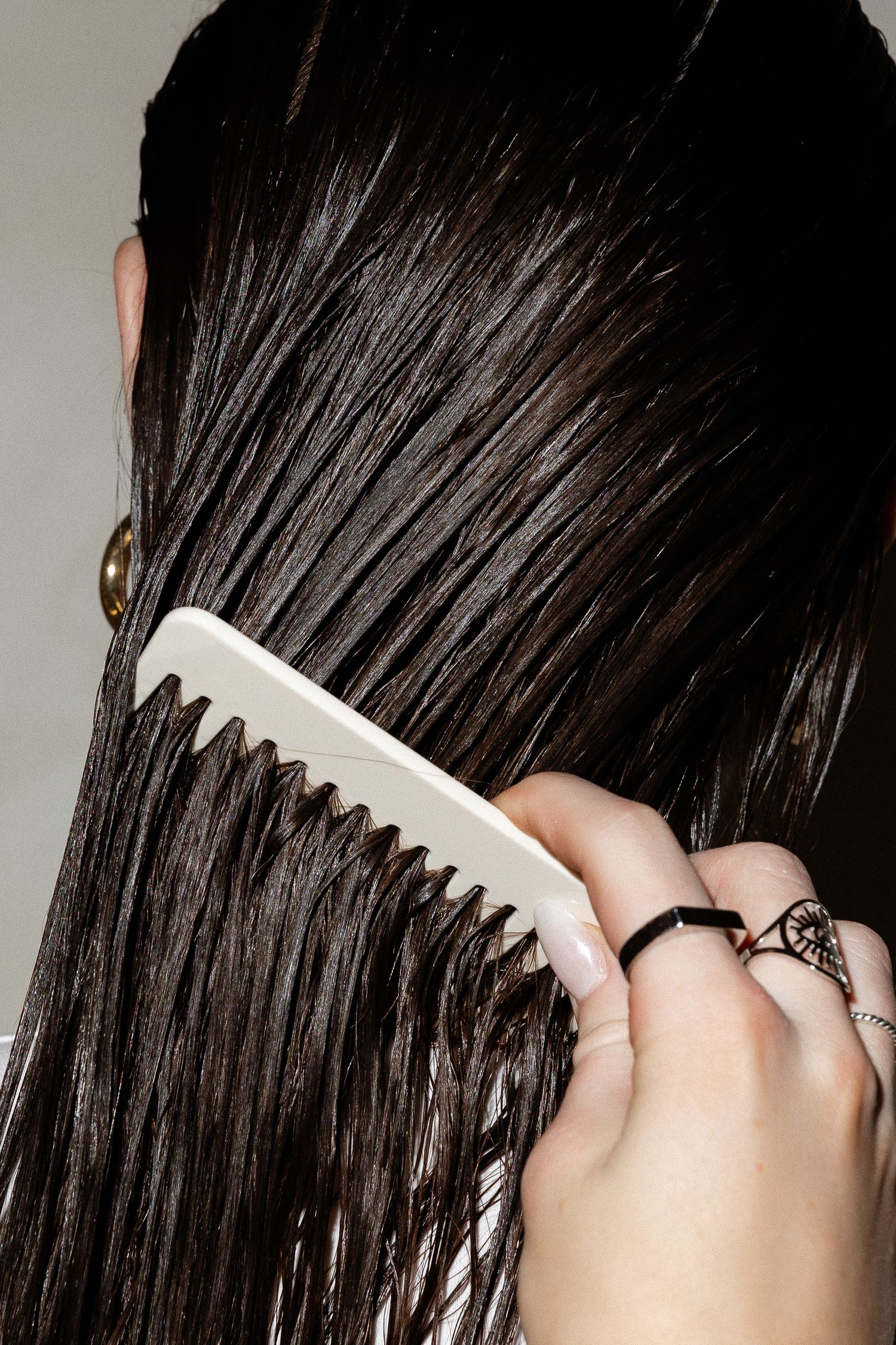 Close-up of combing through straight dark wet hair with white comb.