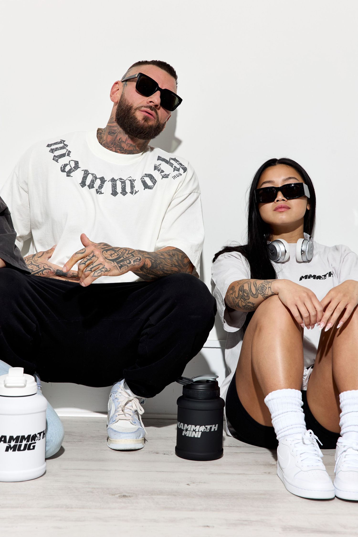 Models in Mammoth streetwear sitting casually against white wall wearing sunglasses.