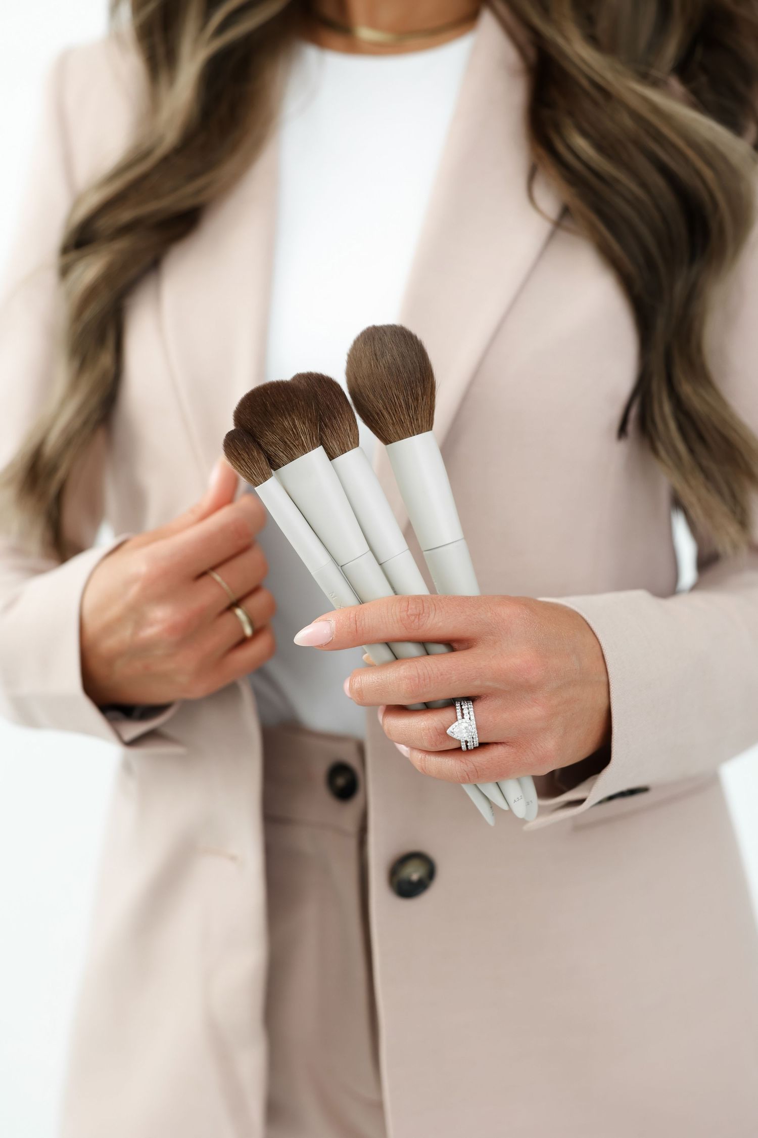 Close-up shots of hands holding makeup brushes wearing pink blazer.