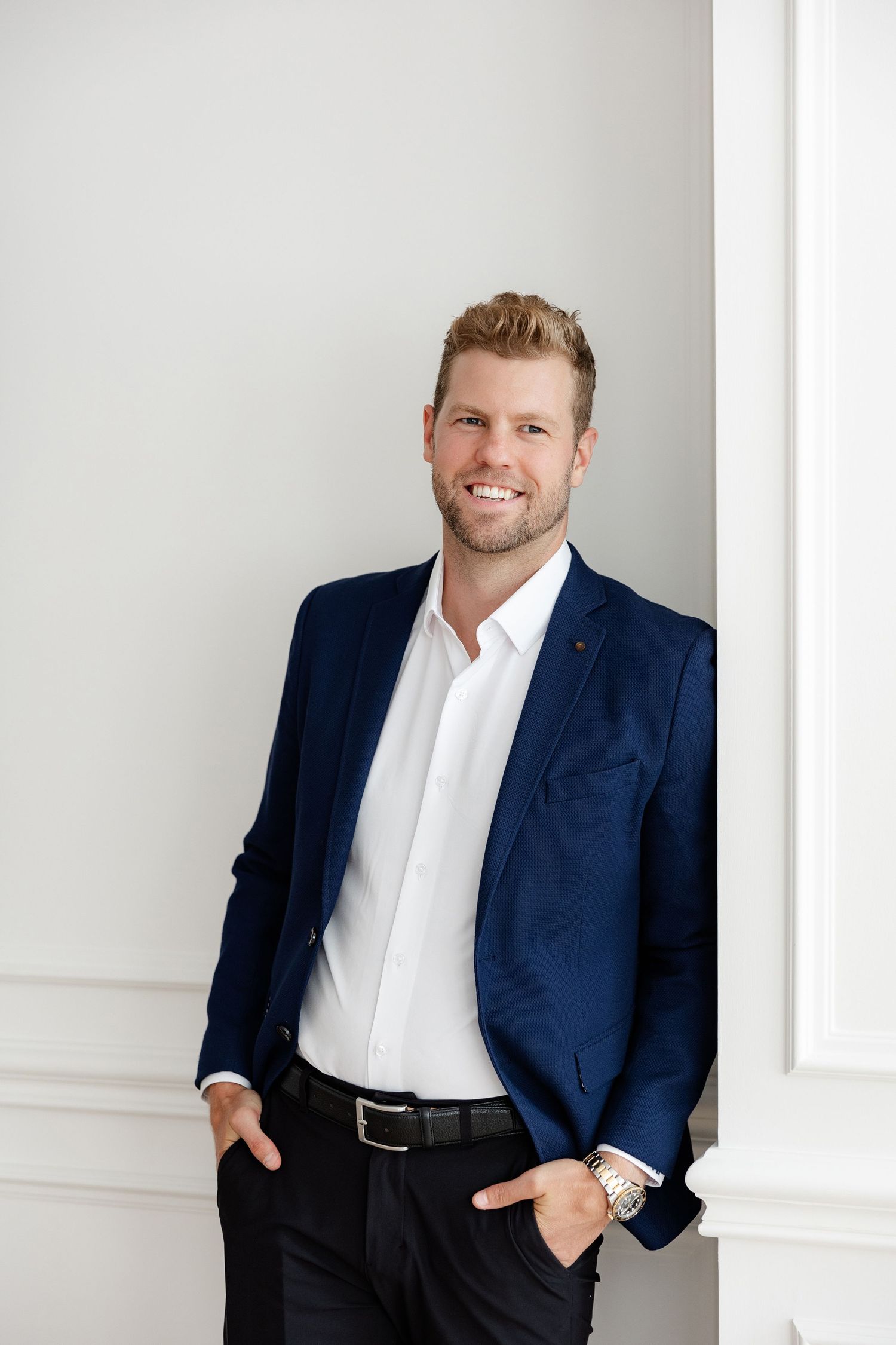 Professional headshot of person in navy suit jacket and white shirt against light background.