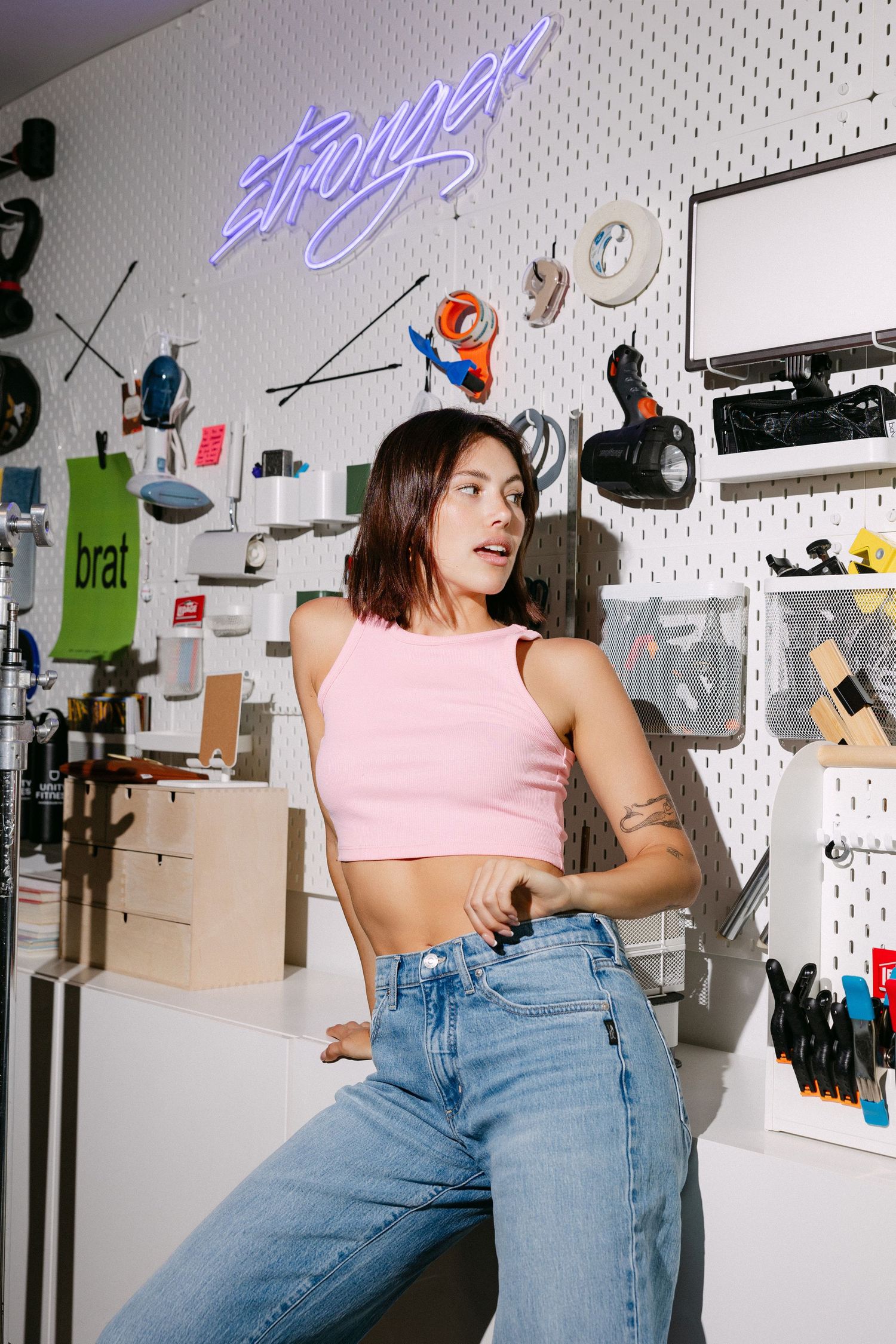 Pink crop top and jeans outfit against pegboard wall with neon sign.