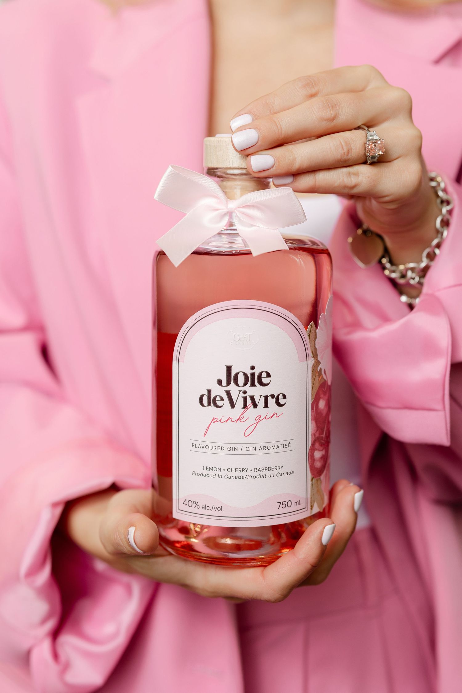 Bottle of Joie de Vivre pink beverage with white bow against pink background.
