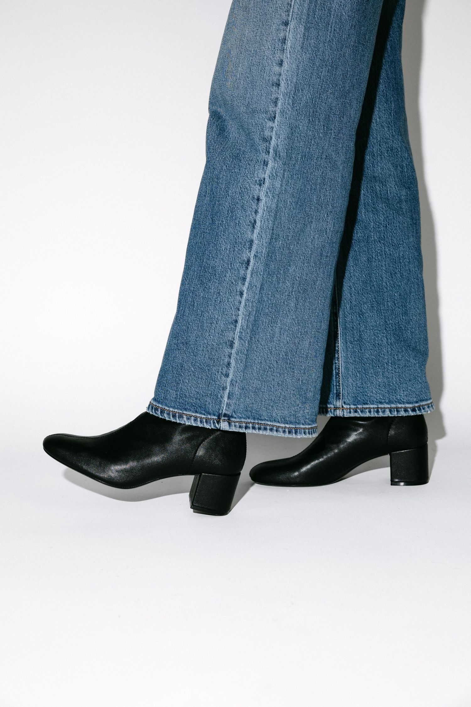 Low angle shot of flared blue jeans with black ankle boots on white background.