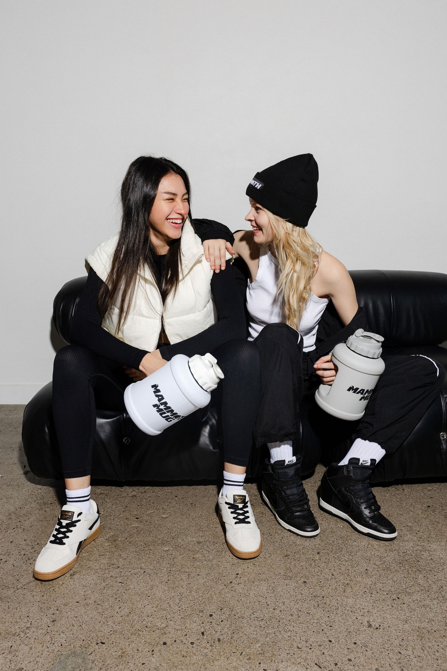 Two people in casual streetwear sit on the floor laughing and interacting with branded containers.