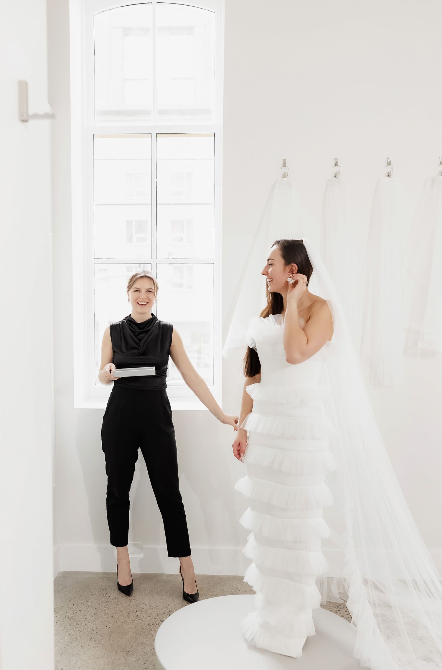 A bright wedding dress fitting session with stylist and bride in a modern white studio space.