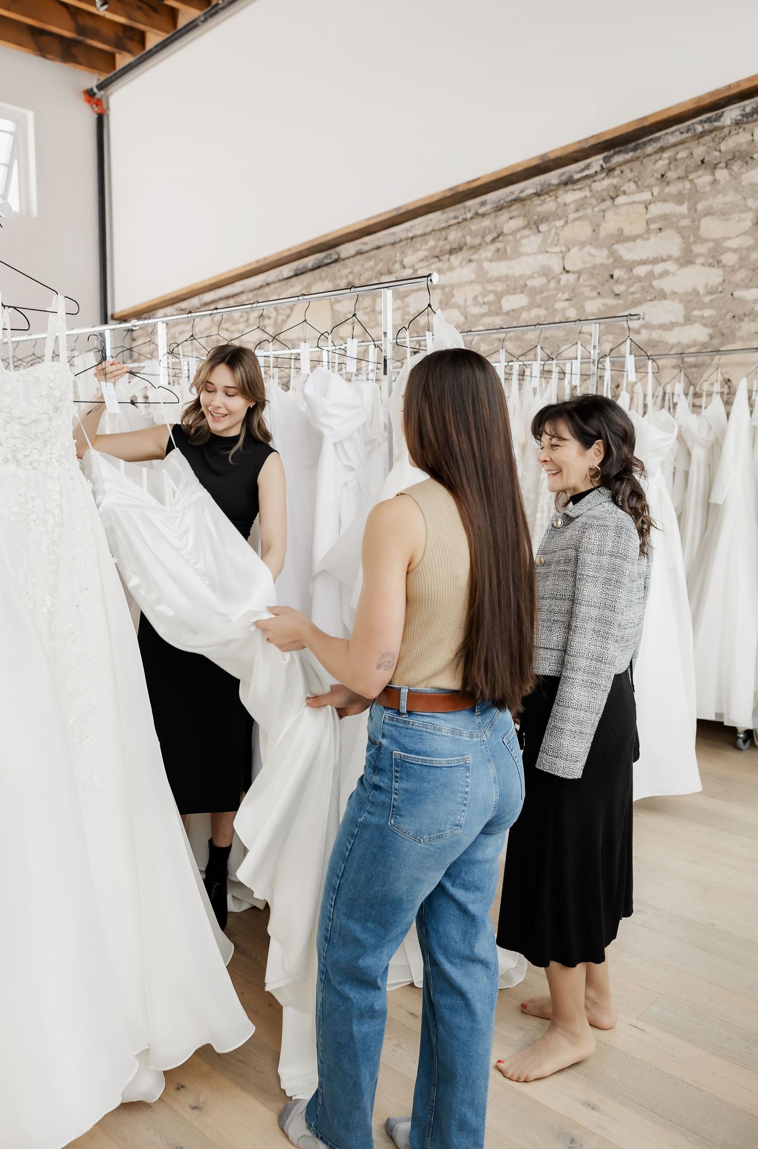 Women browsing through white wedding dresses on display racks in a modern bridal shop.