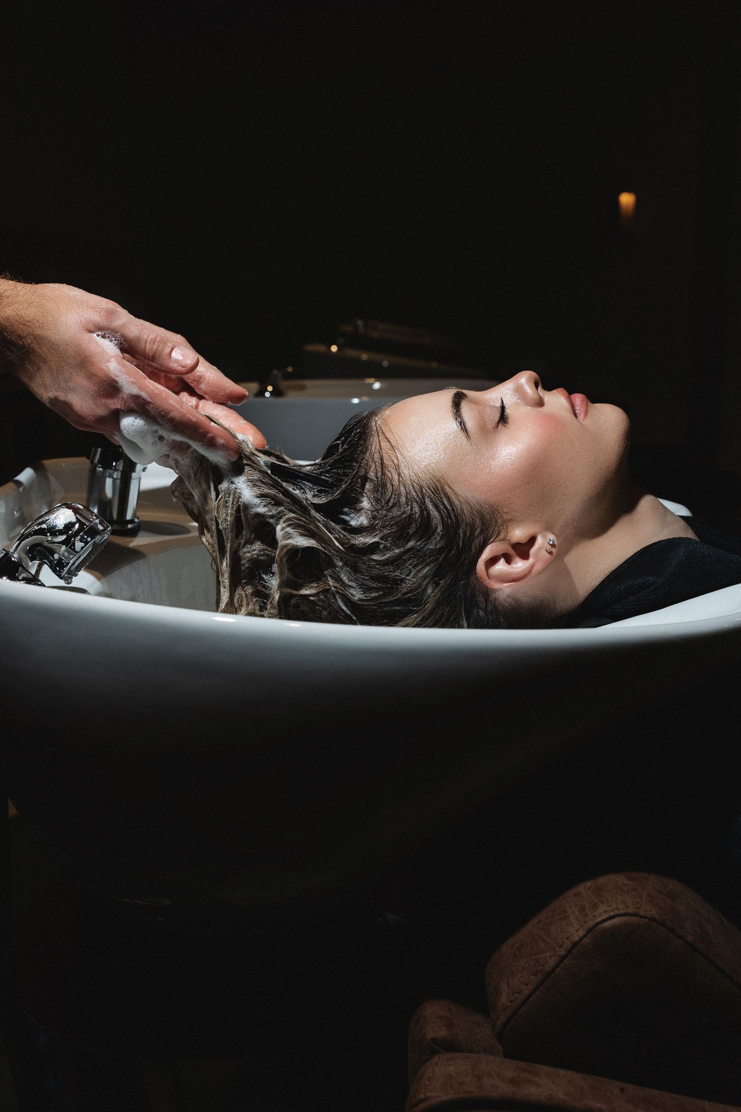Dark wet hair being washed in dramatic lighting against black background.