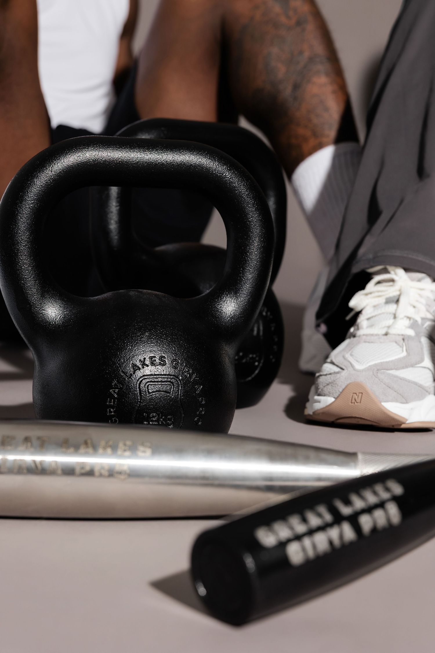 Black kettlebell and white athletic shoes on gray surface with exercise equipment.