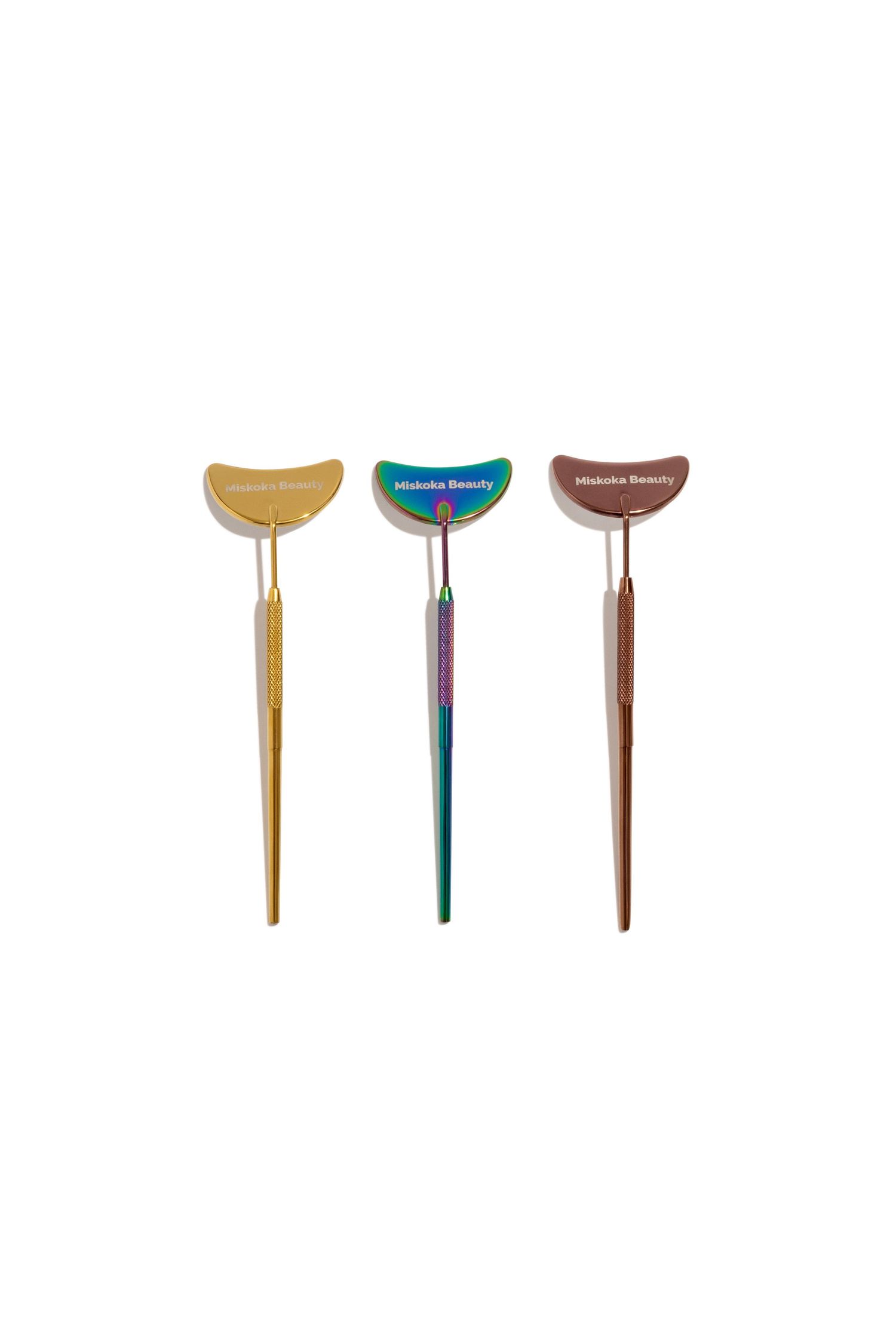 Three colorful makeup brushes with crescent-shaped handles in gold, teal, and bronze.