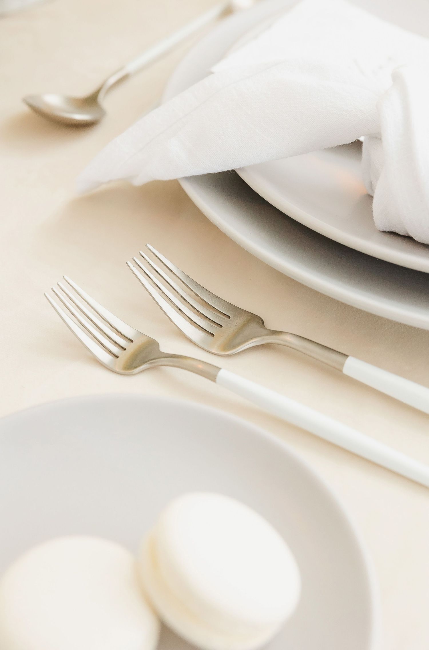 Close-up of elegant white place setting with silver forks and macarons on plate.