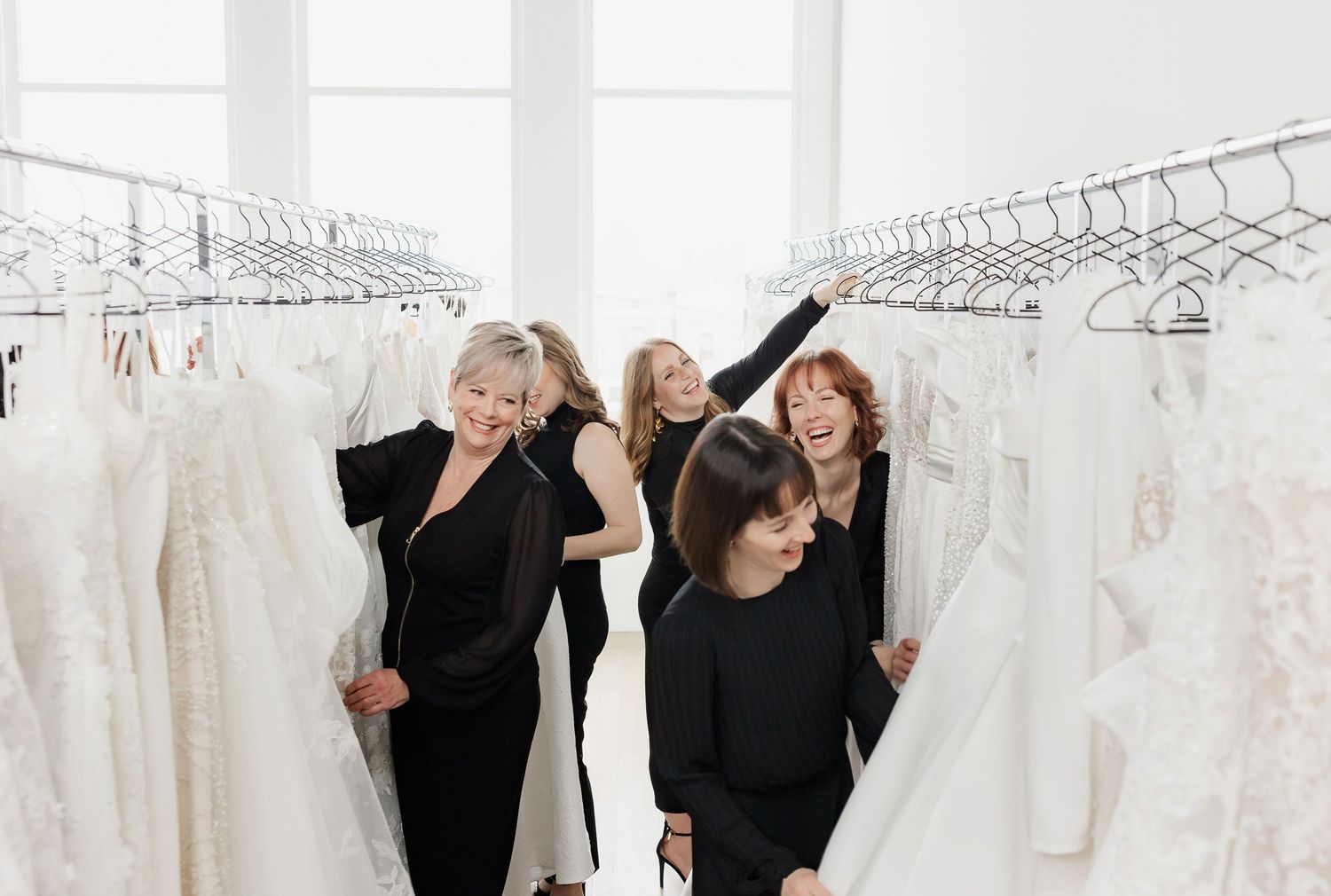 Staff members browsing through white wedding dresses hanging on racks in a bright boutique.