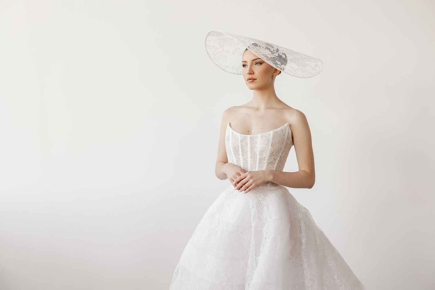 Ethereal bridal portrait featuring flowing tulle dress and statement hat against white backdrop.
