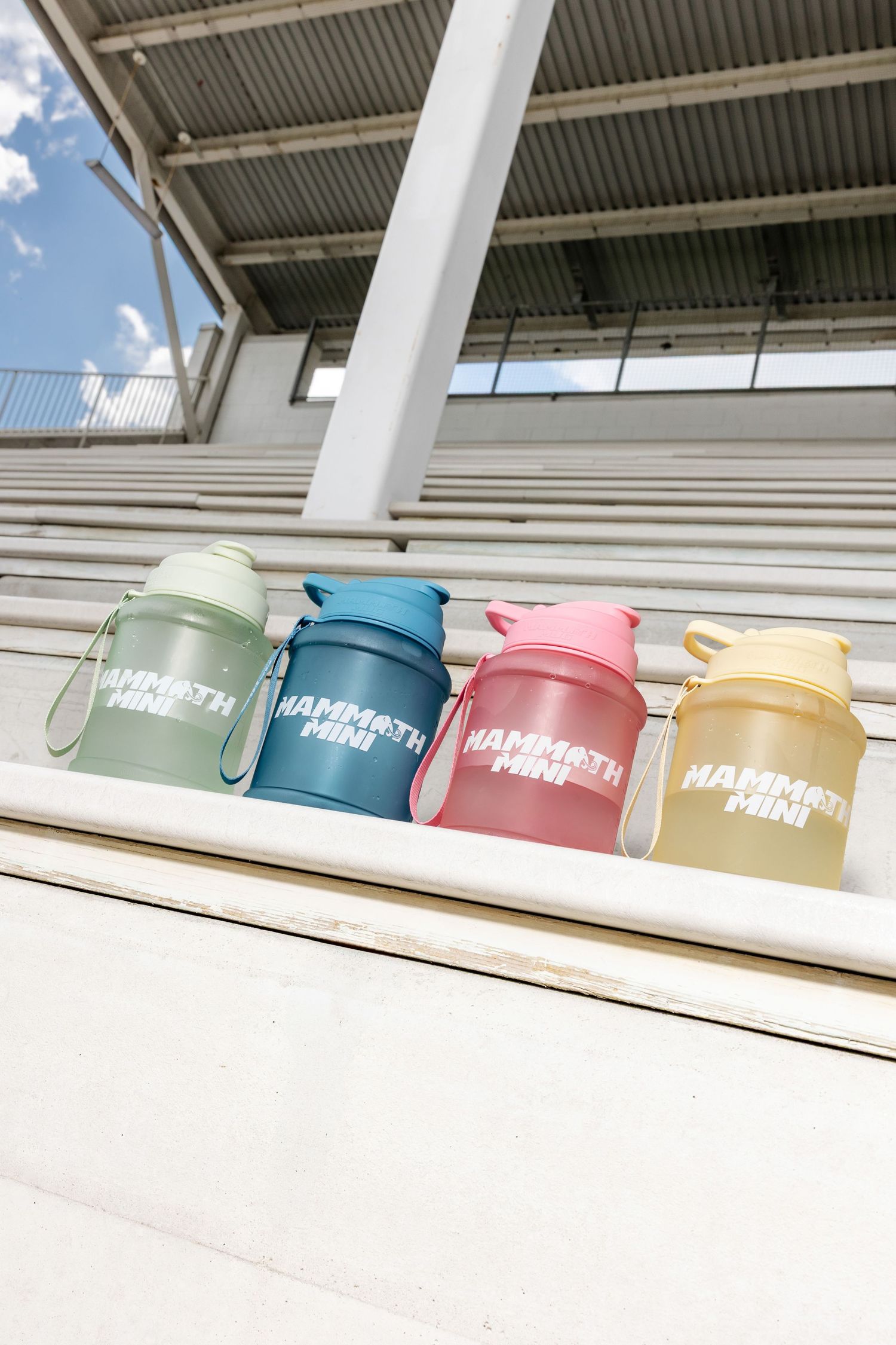 Collection of pastel colored water bottles displayed on white surface under outdoor covering.
