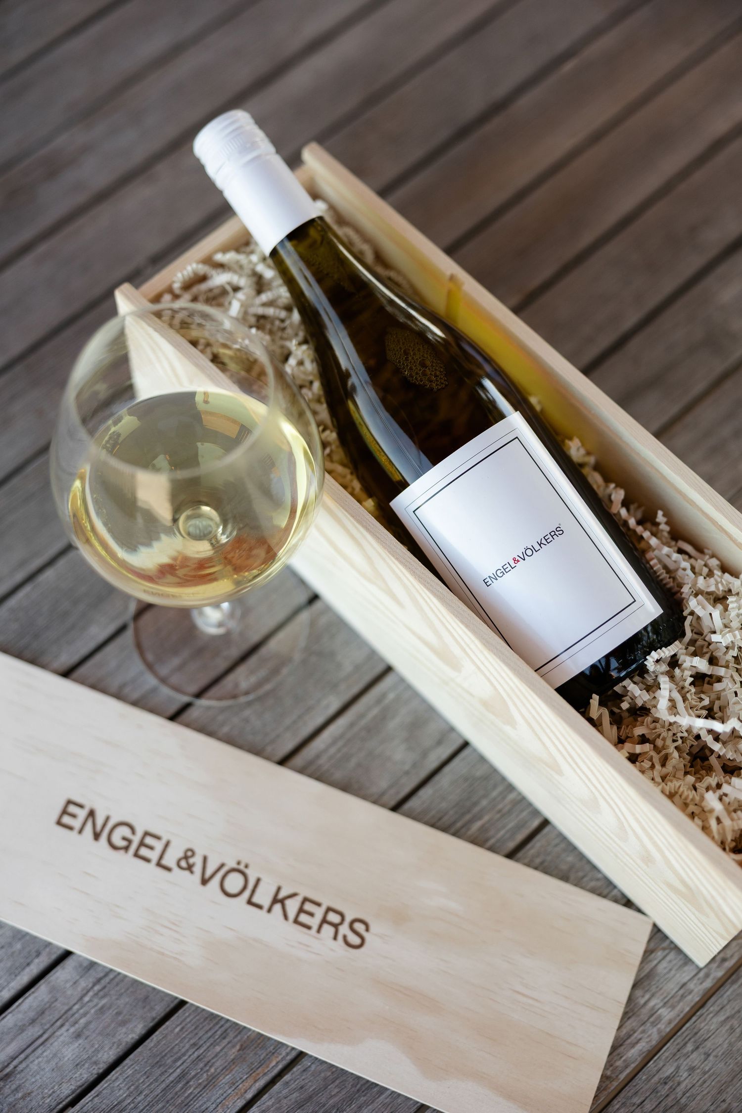 Wine bottle nestled in wooden presentation box with decorative packaging material.