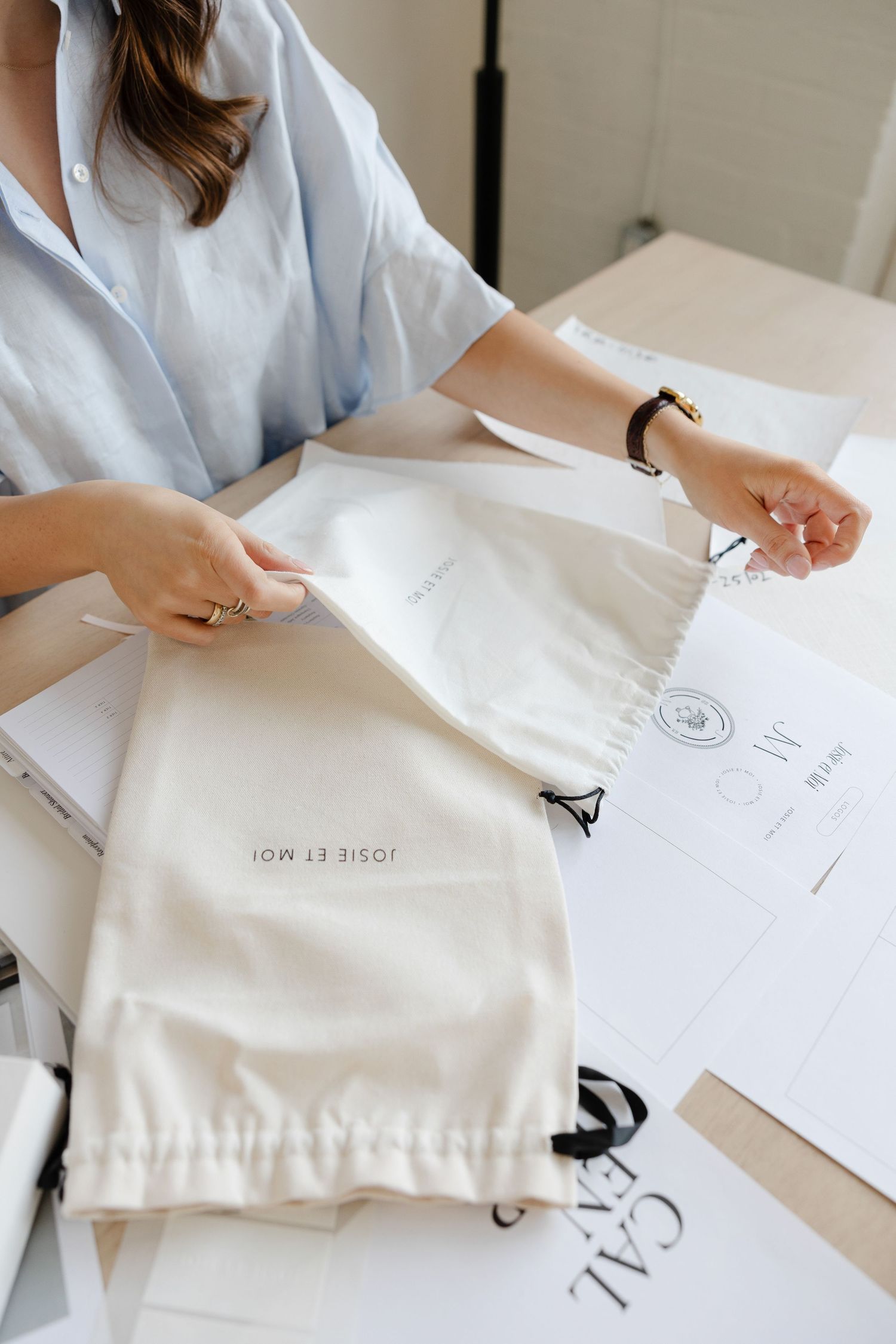 Hands arranging white branded bags and paper materials on desk surface.