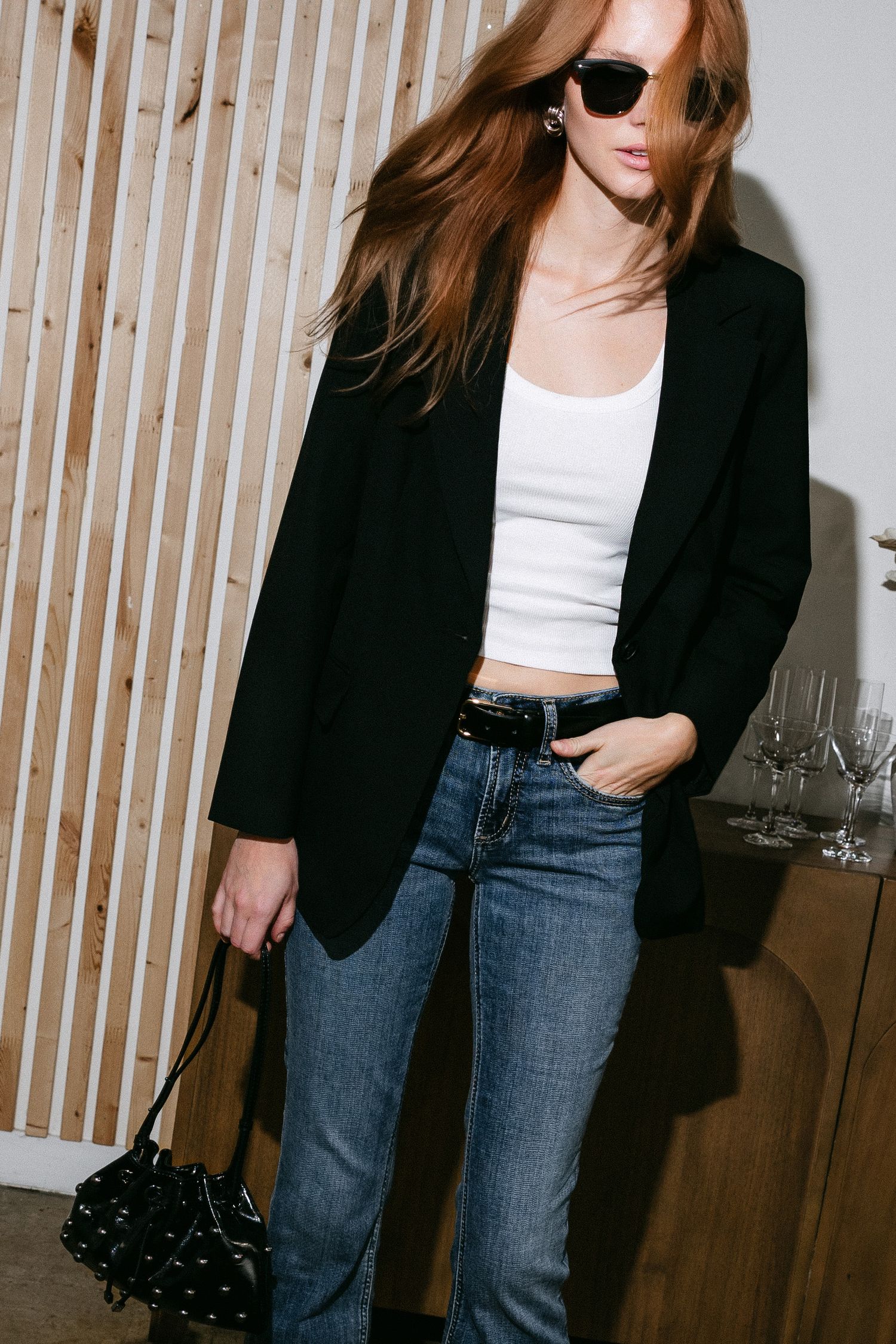 Stylish outfit featuring black blazer, white crop top, jeans and sunglasses with a casual yet sophisticated look.