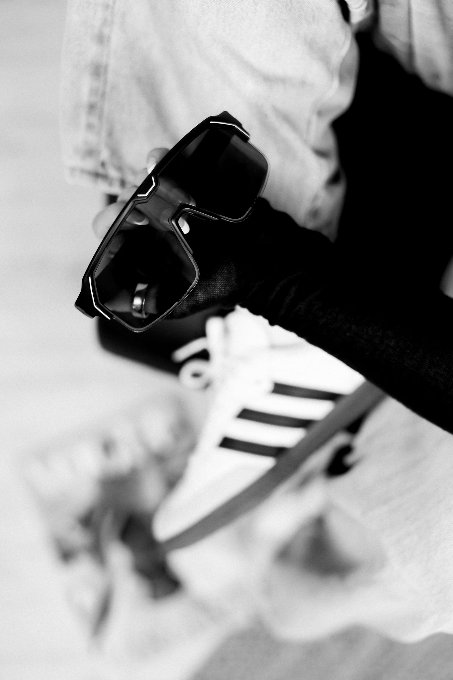 Black sunglasses and white sneaker shown in artistic black and white composition.