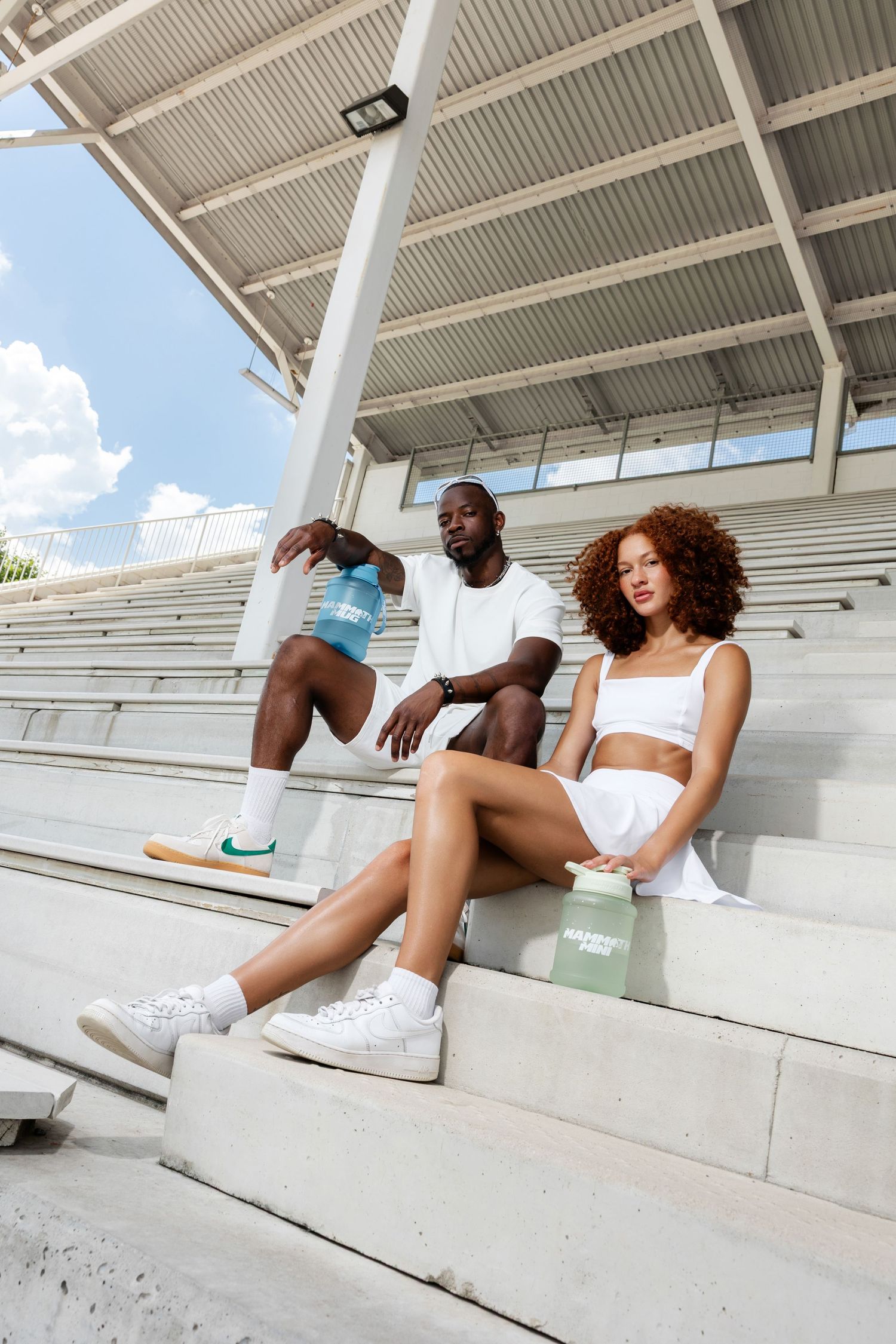 People relaxing on concrete bleachers with water bottles during a sunny day.
