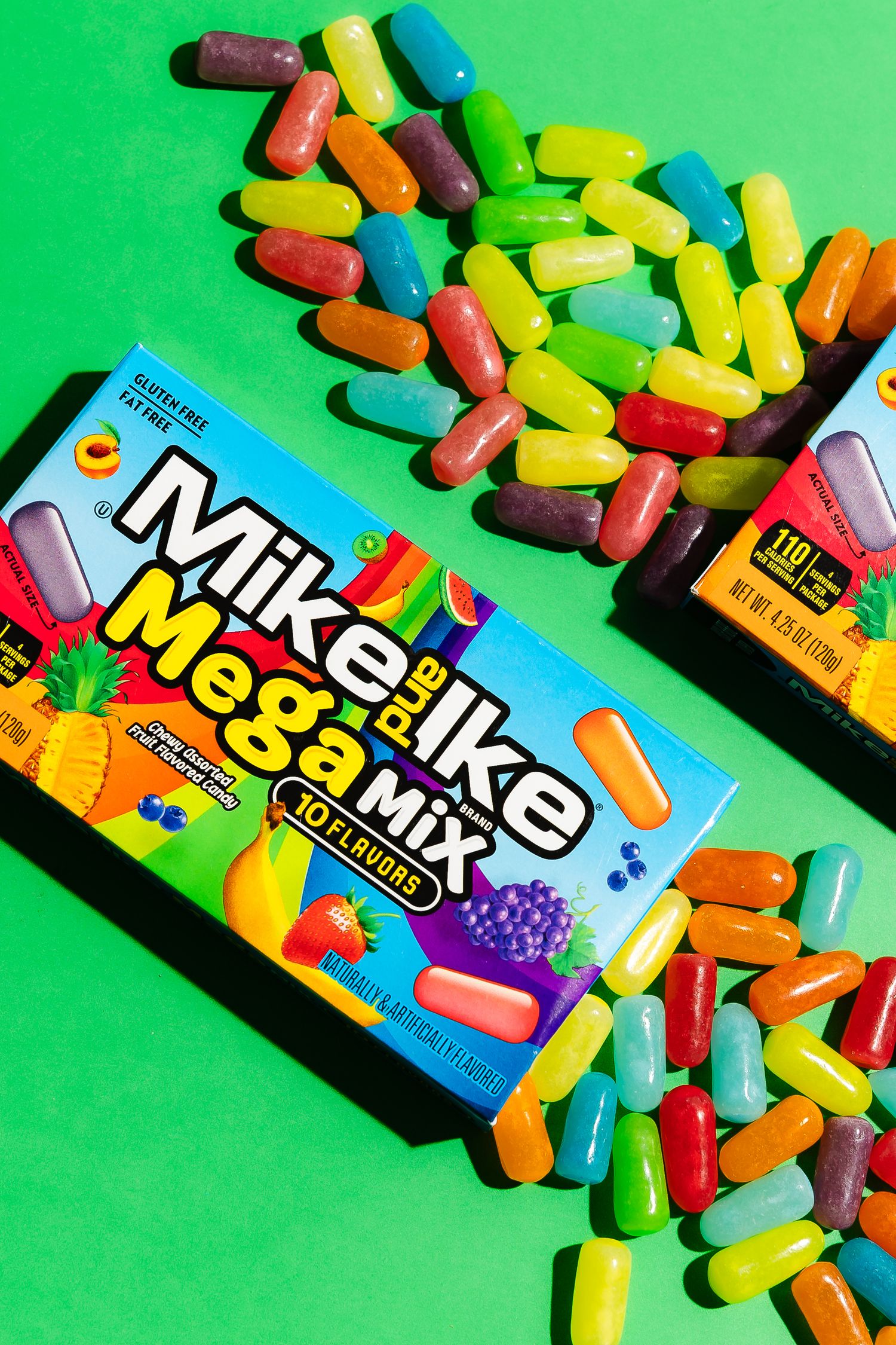 Colorful Mike and Ike Mega Mix candies scattered around box on green background.