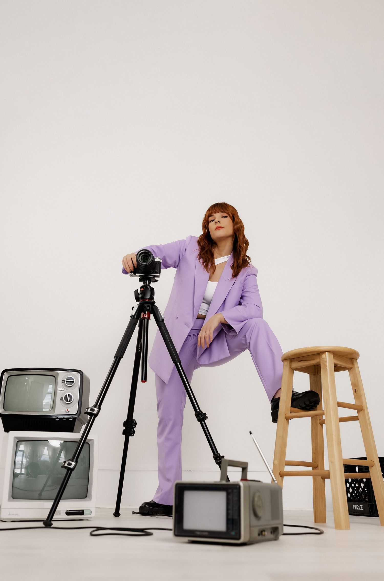Fashion photography setup with vintage TVs, tripod, and purple suit against white backdrop.