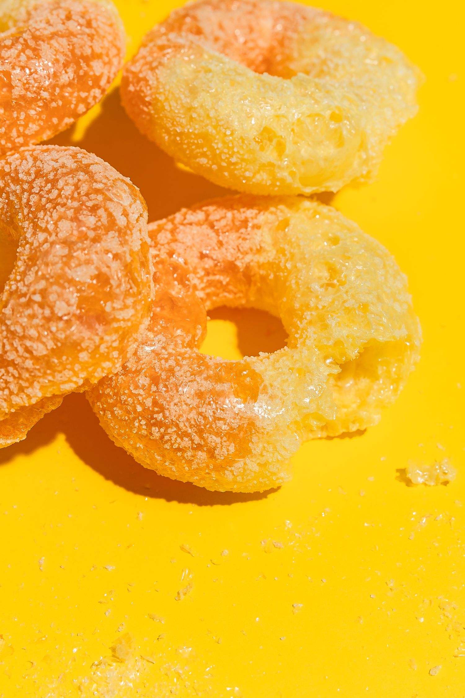 Orange sugar-coated gummy candies on bright yellow background.