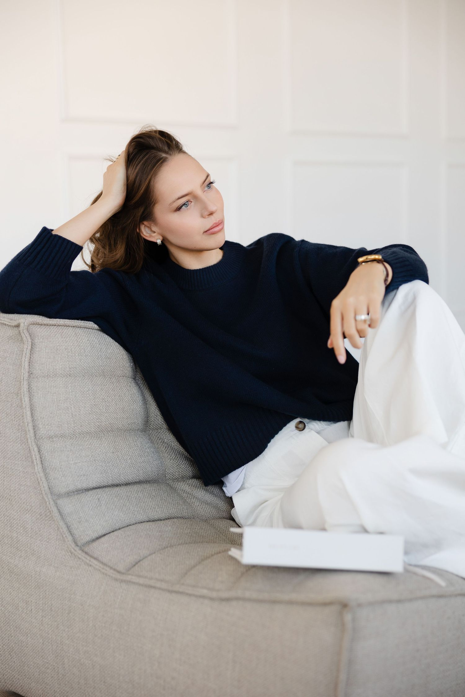 Relaxed lifestyle portrait of woman in navy sweater lounging on grey couch.