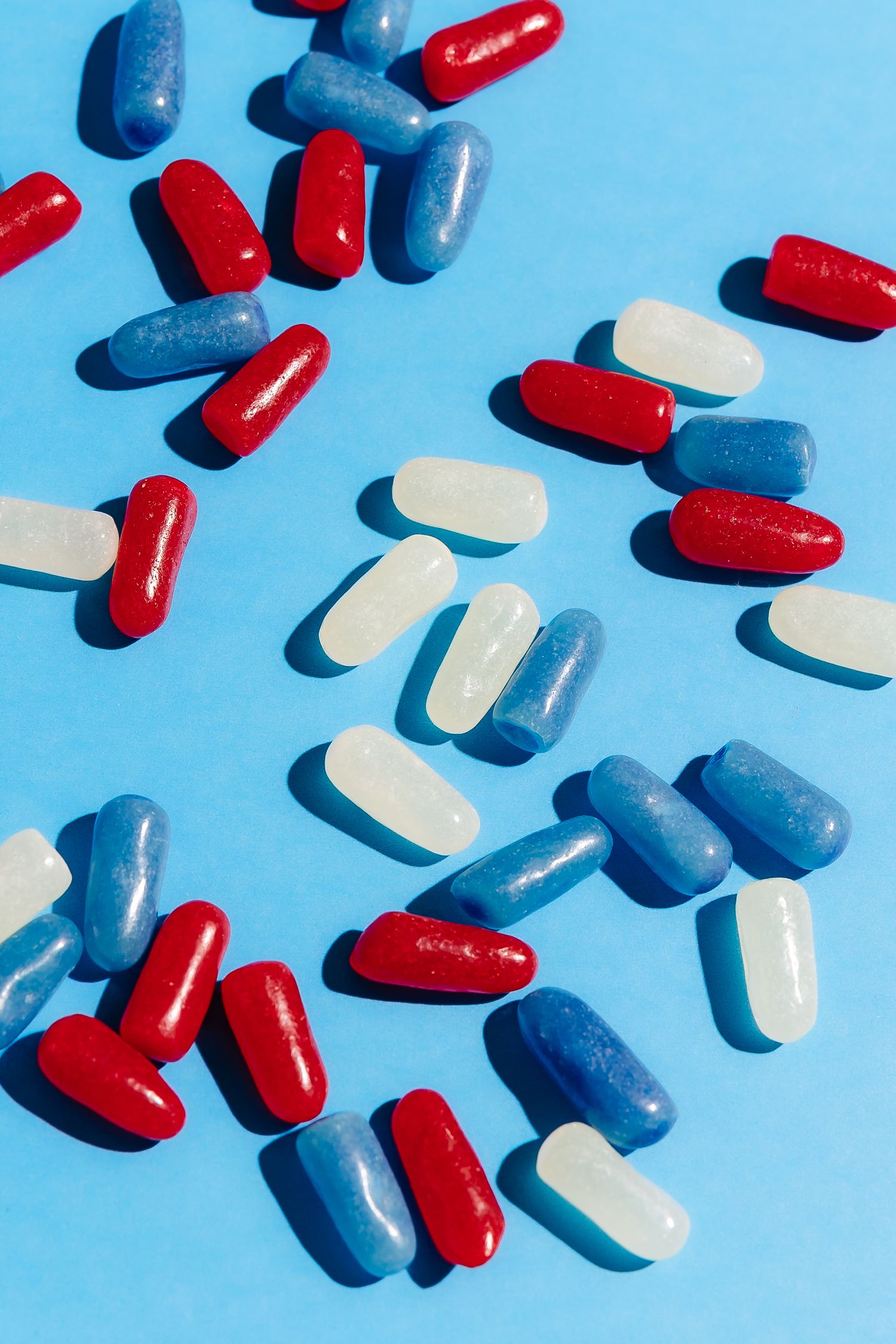 Red, white and blue capsule pills scattered on bright blue background.