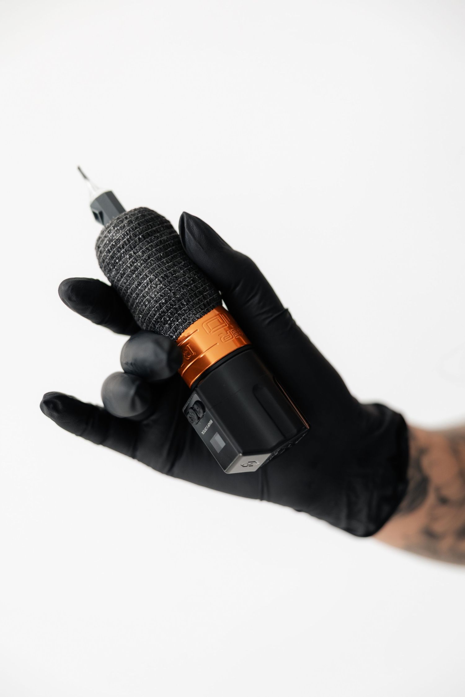 Tattooed hand wearing black glove holding tattoo machine with copper accent.