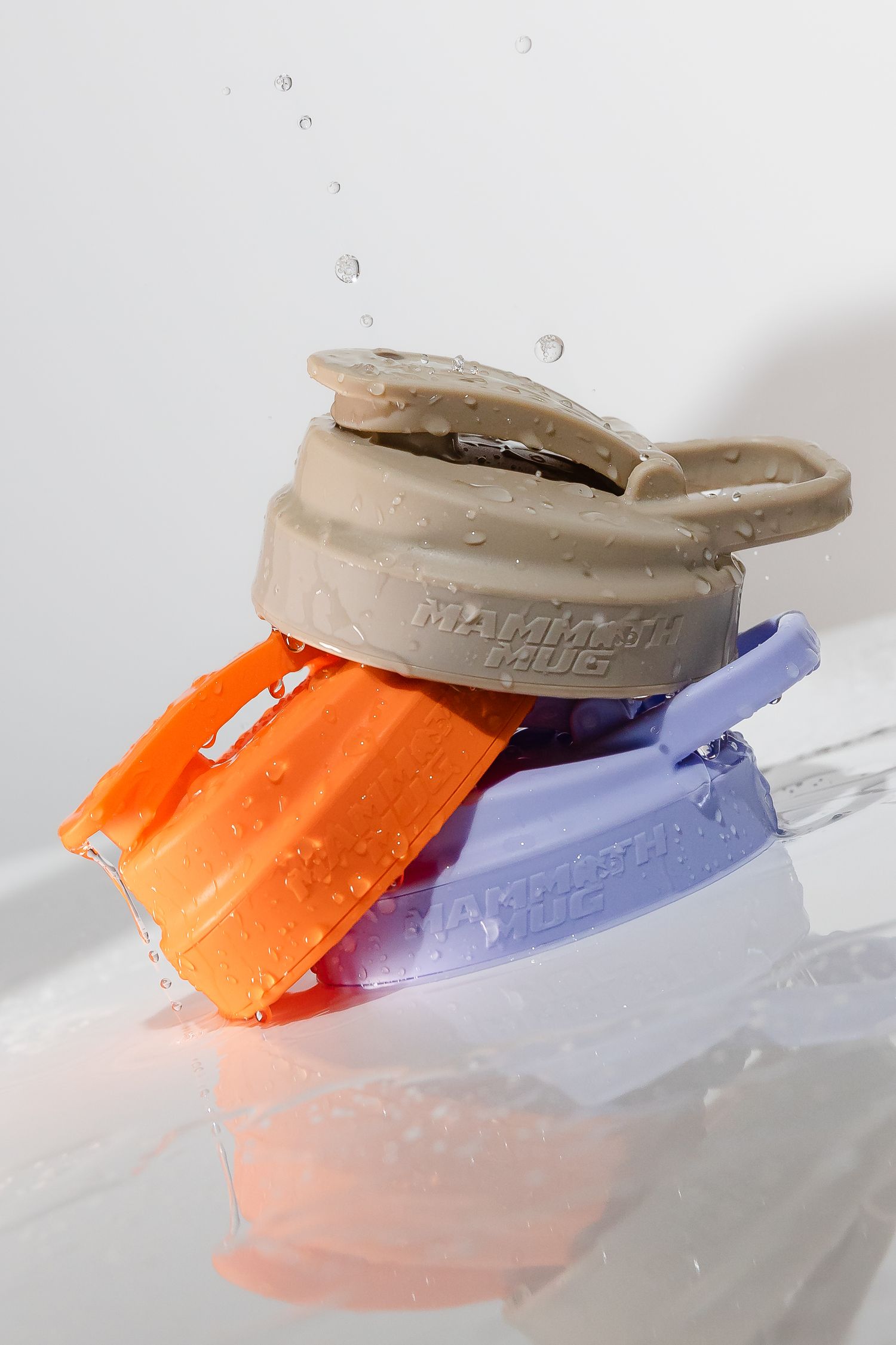 Three wet Mammoth Mini shaker bottles in beige, orange and purple colors on reflective surface.
