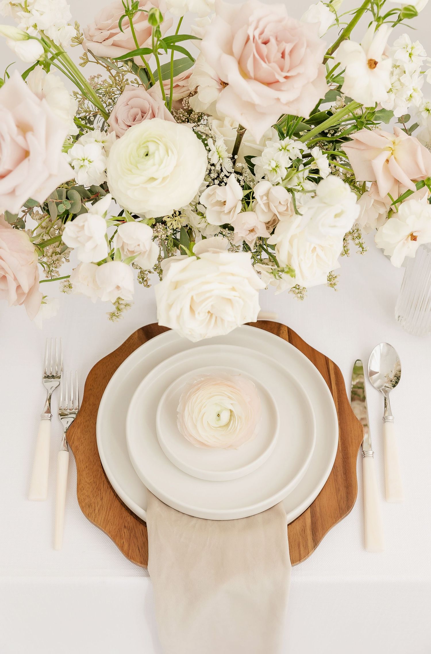 Romantic place setting with white and pink roses above stacked plates on wooden charger.