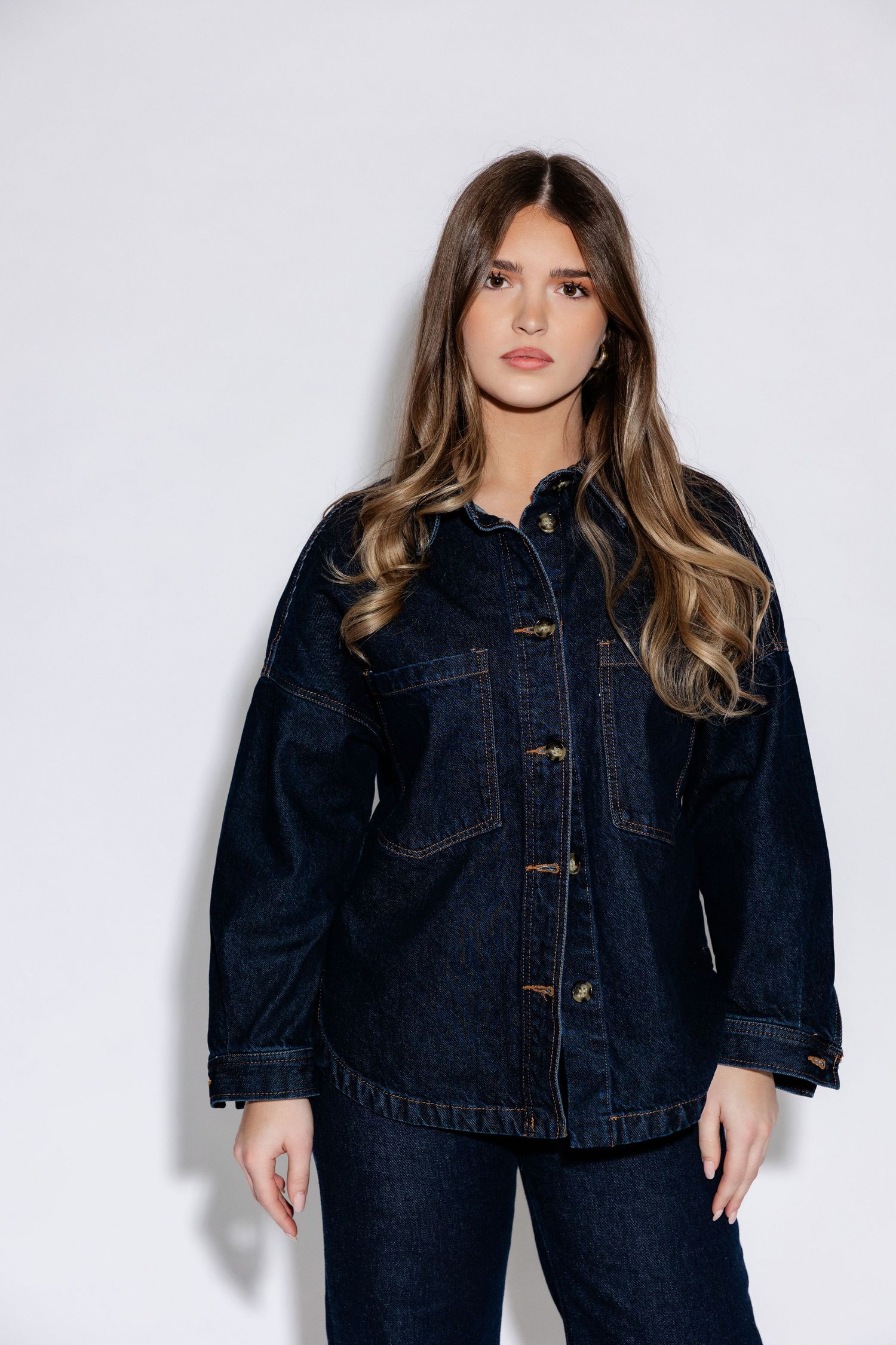 Model wearing dark denim jacket and jeans ensemble against white background.