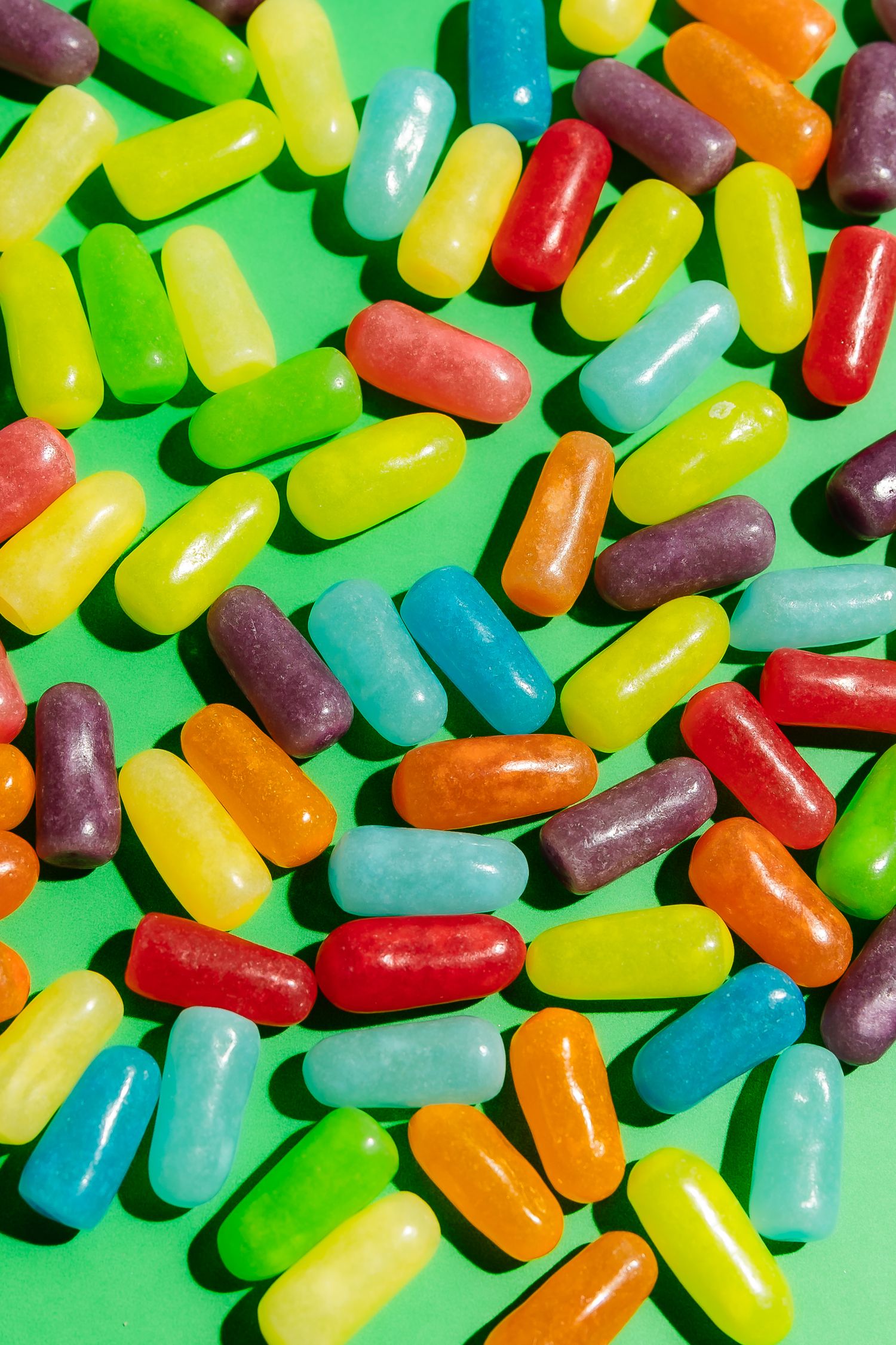Colorful jelly bean candies scattered on bright green background.