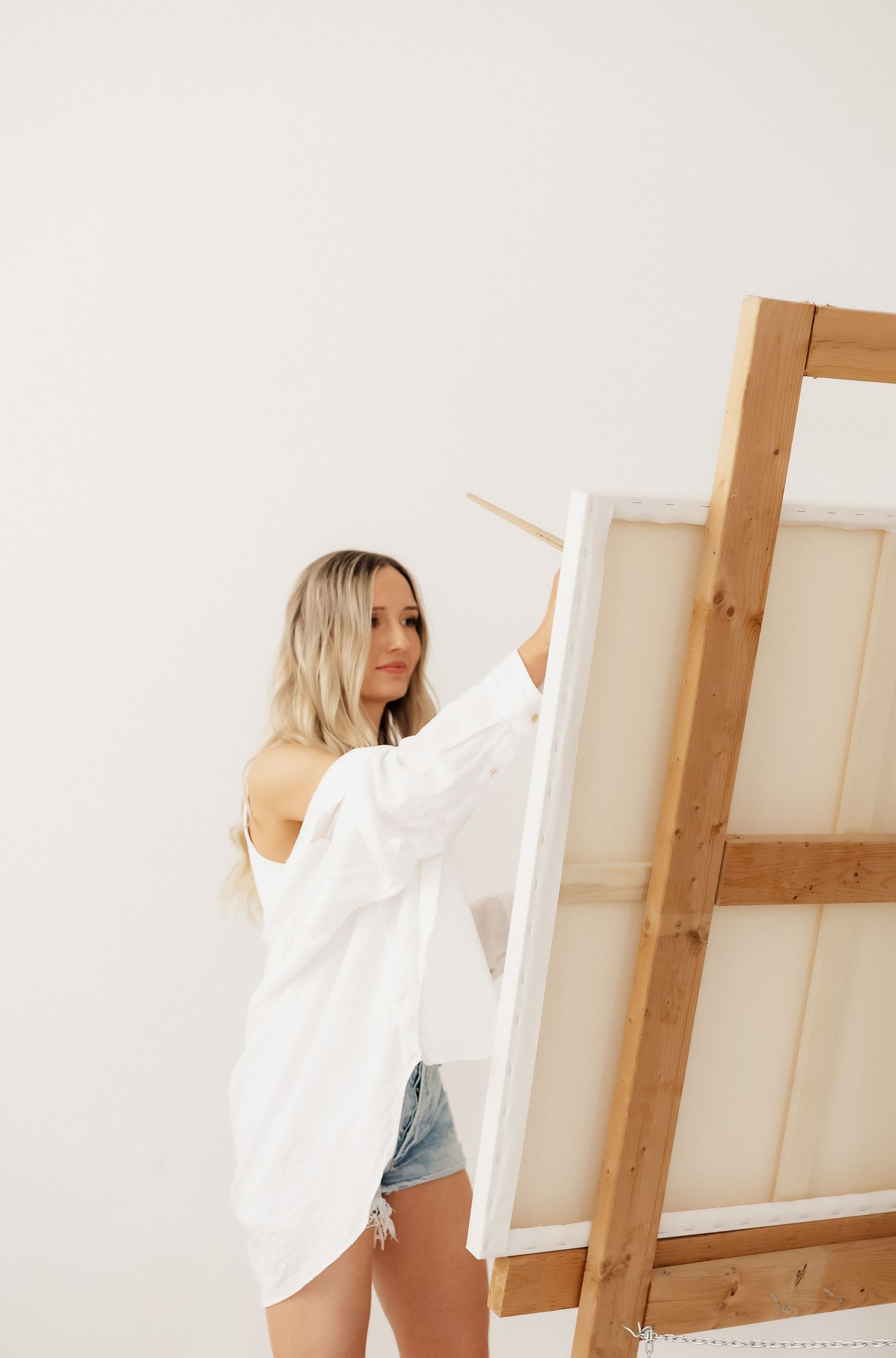 Artist in white shirt and denim moving dynamically in studio with wooden easel.