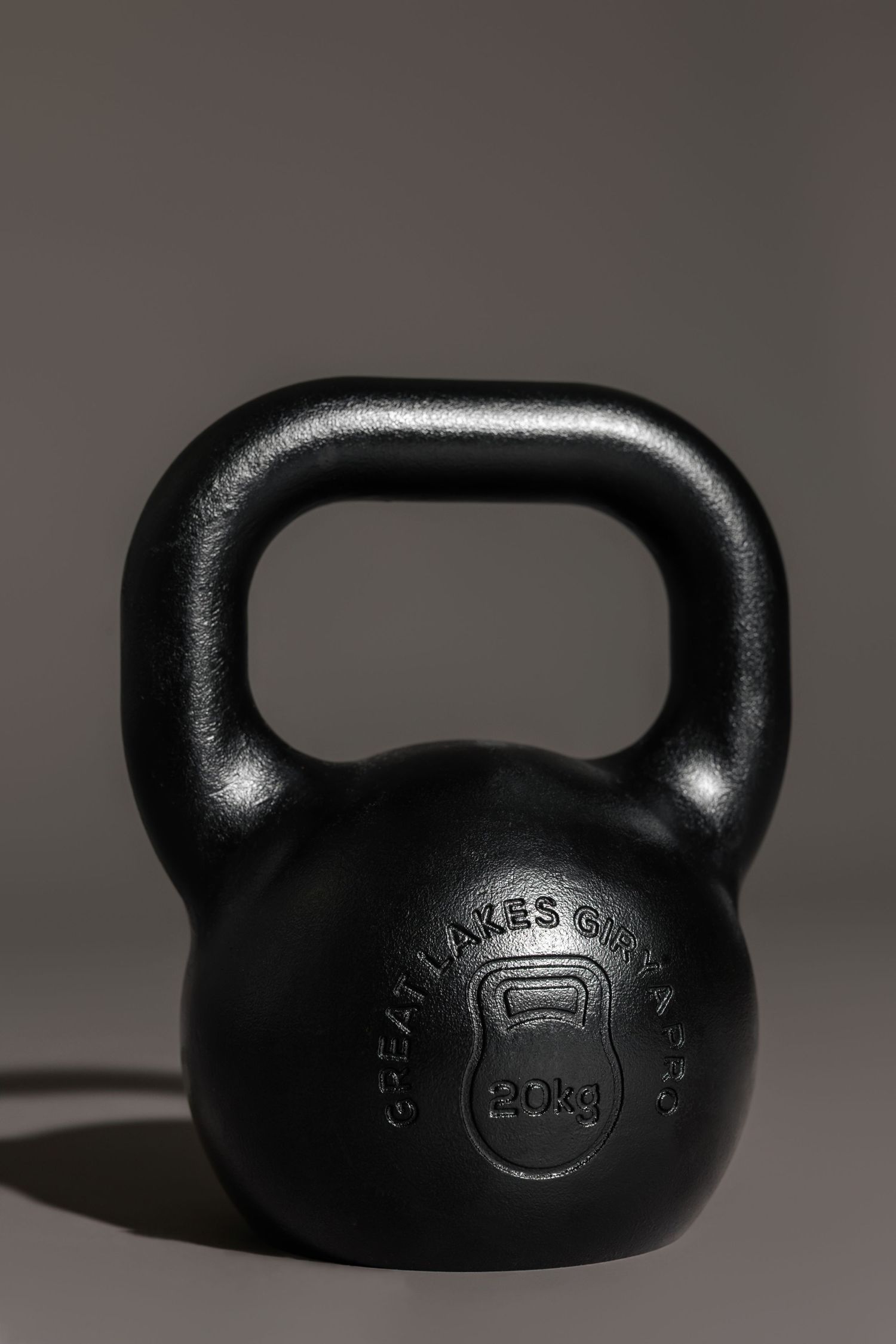 Black cast iron kettlebell photographed against grey background.