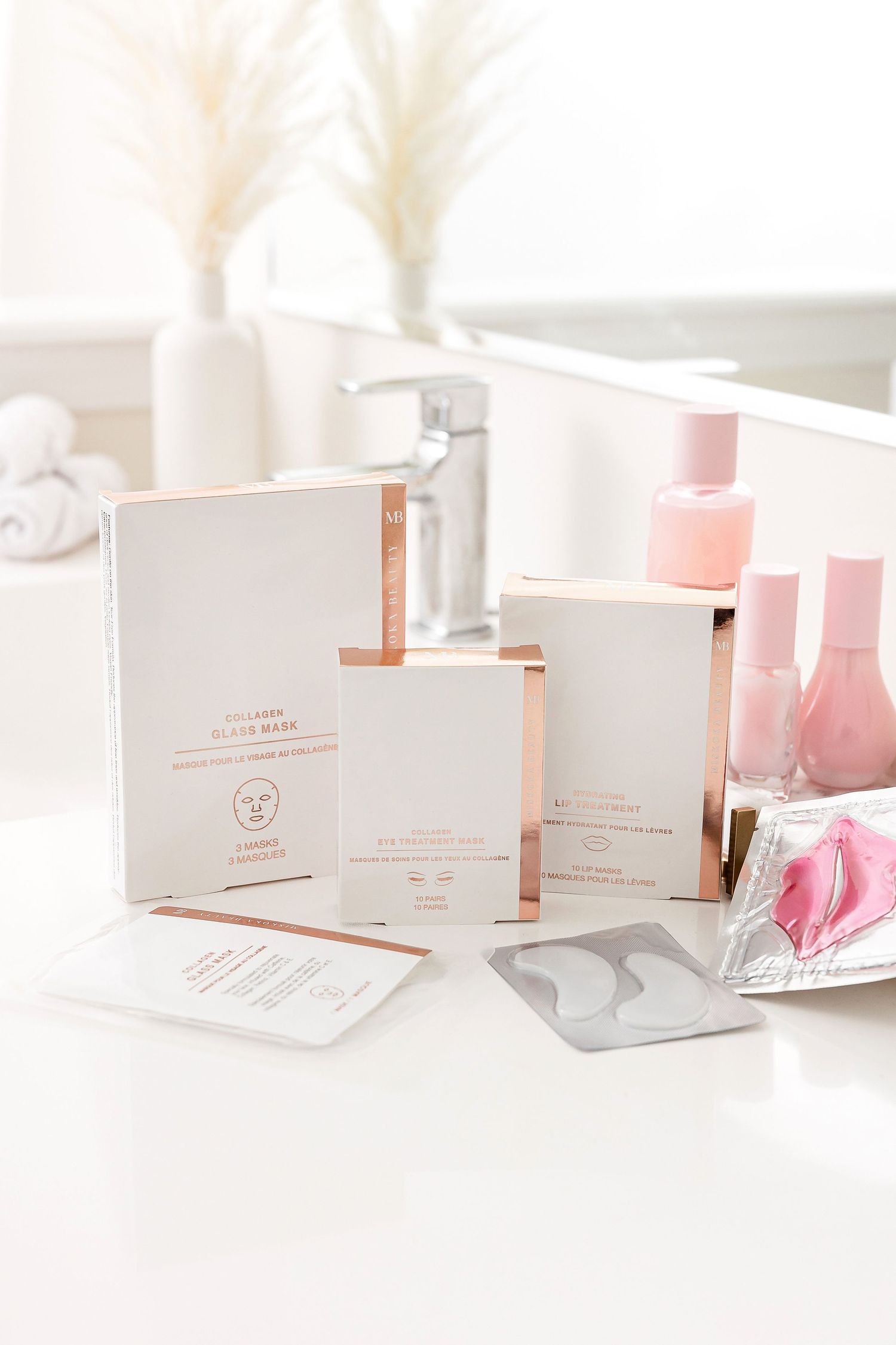 Elegant beauty product display with white and rose gold packaging near pampas grass decor.