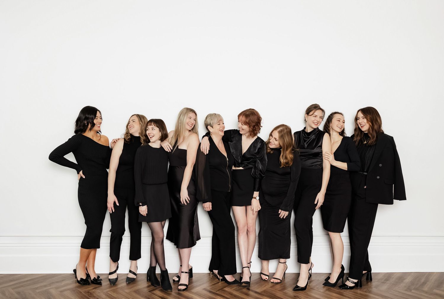 Group of people in black outfits posing playfully against a white wall.