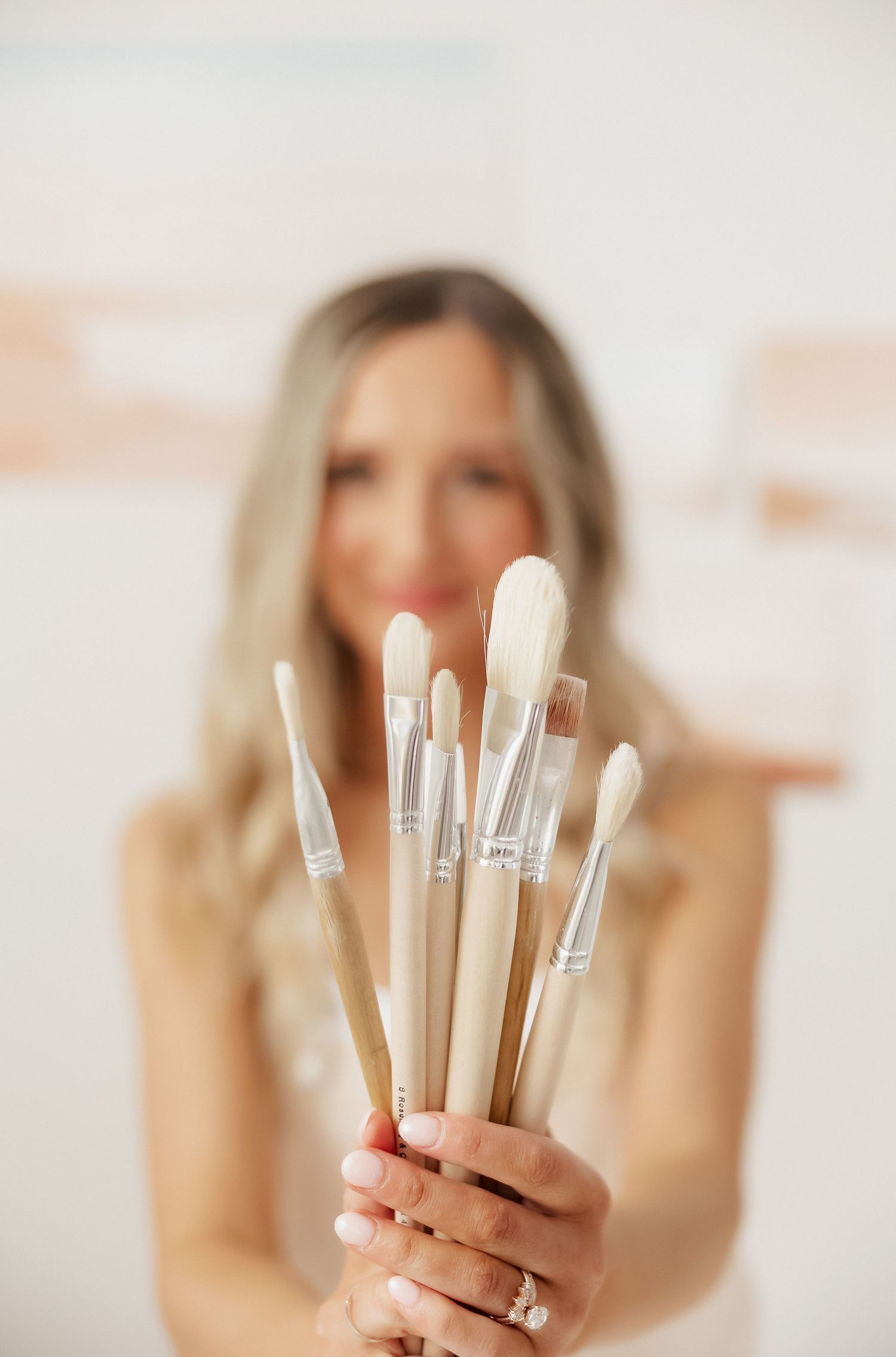 Close-up of hands holding multiple paint brushes against white background.