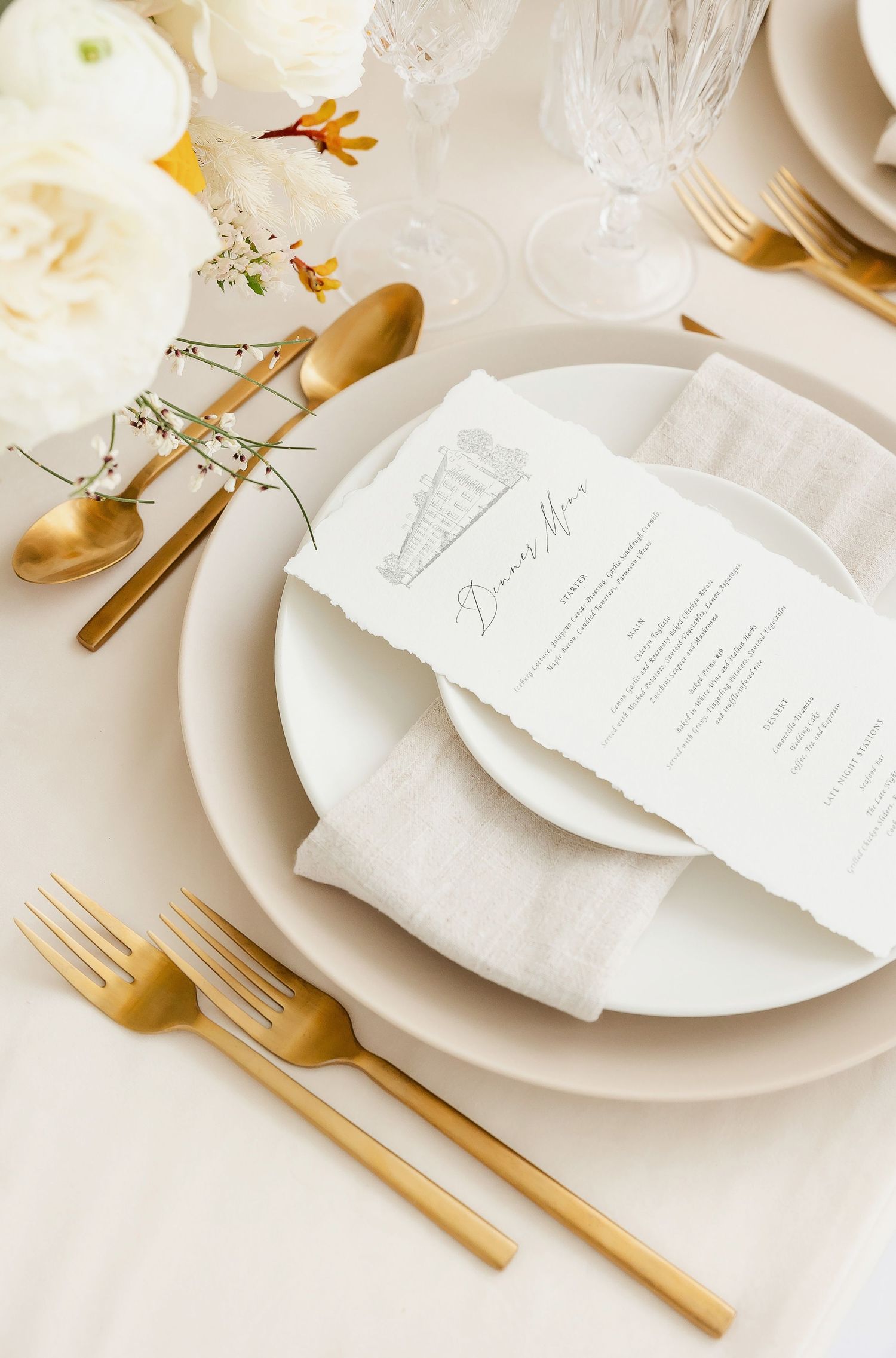 Elegant place setting with gold cutlery, white plates, and a menu card on a light tablecloth.